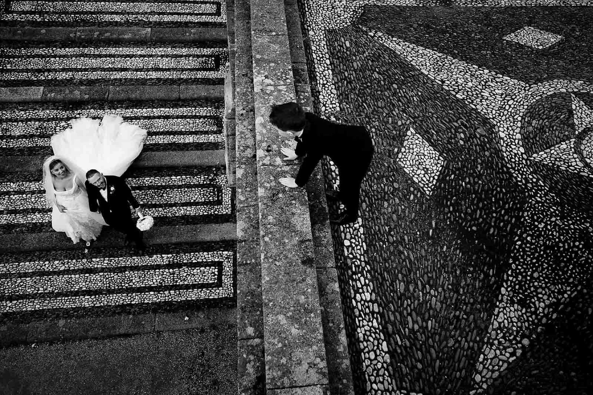 wedding photog of couple photographe3d from above while a kid looks down on them in black and white