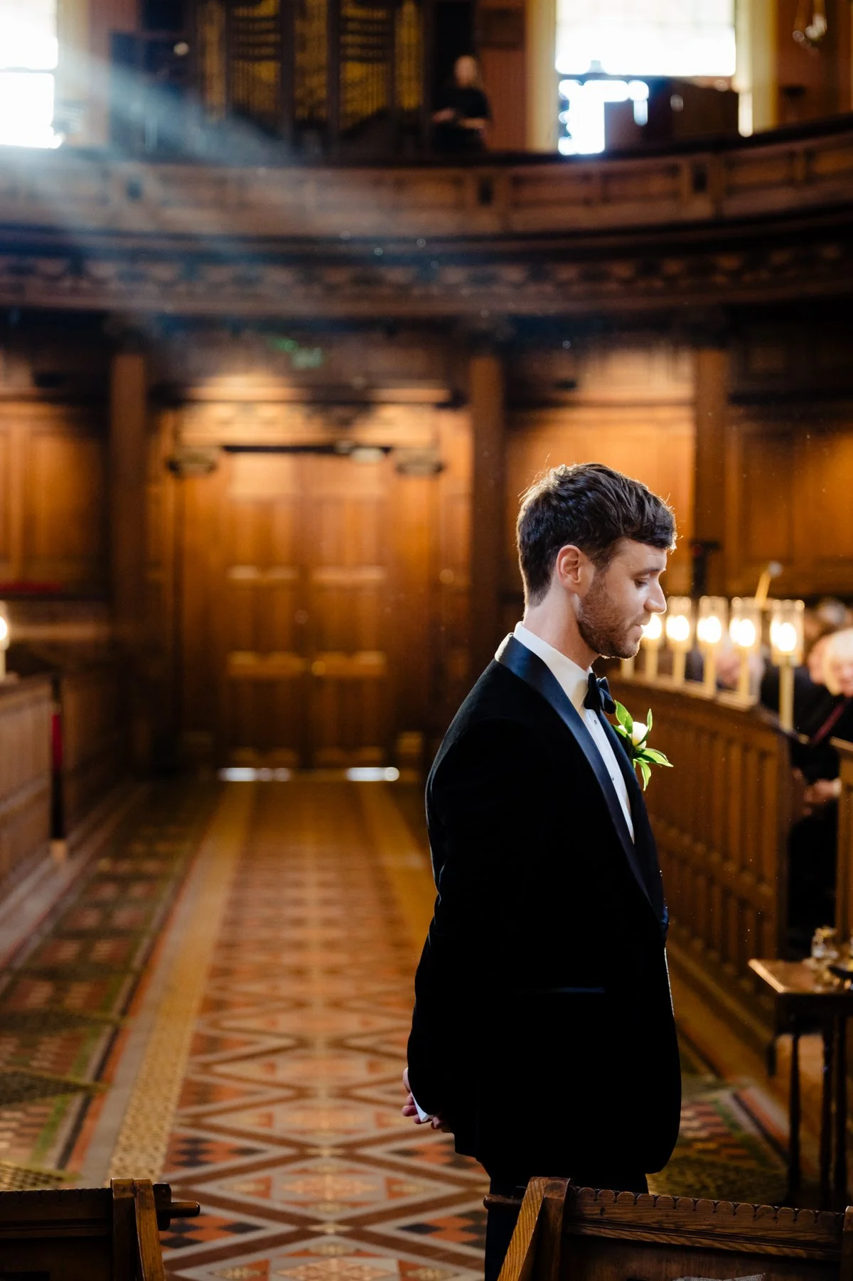 A groom in black tie waits in the trinity college chapel for his bride at this winter wedding in Dublin City centre photographed by Annie Kheffache