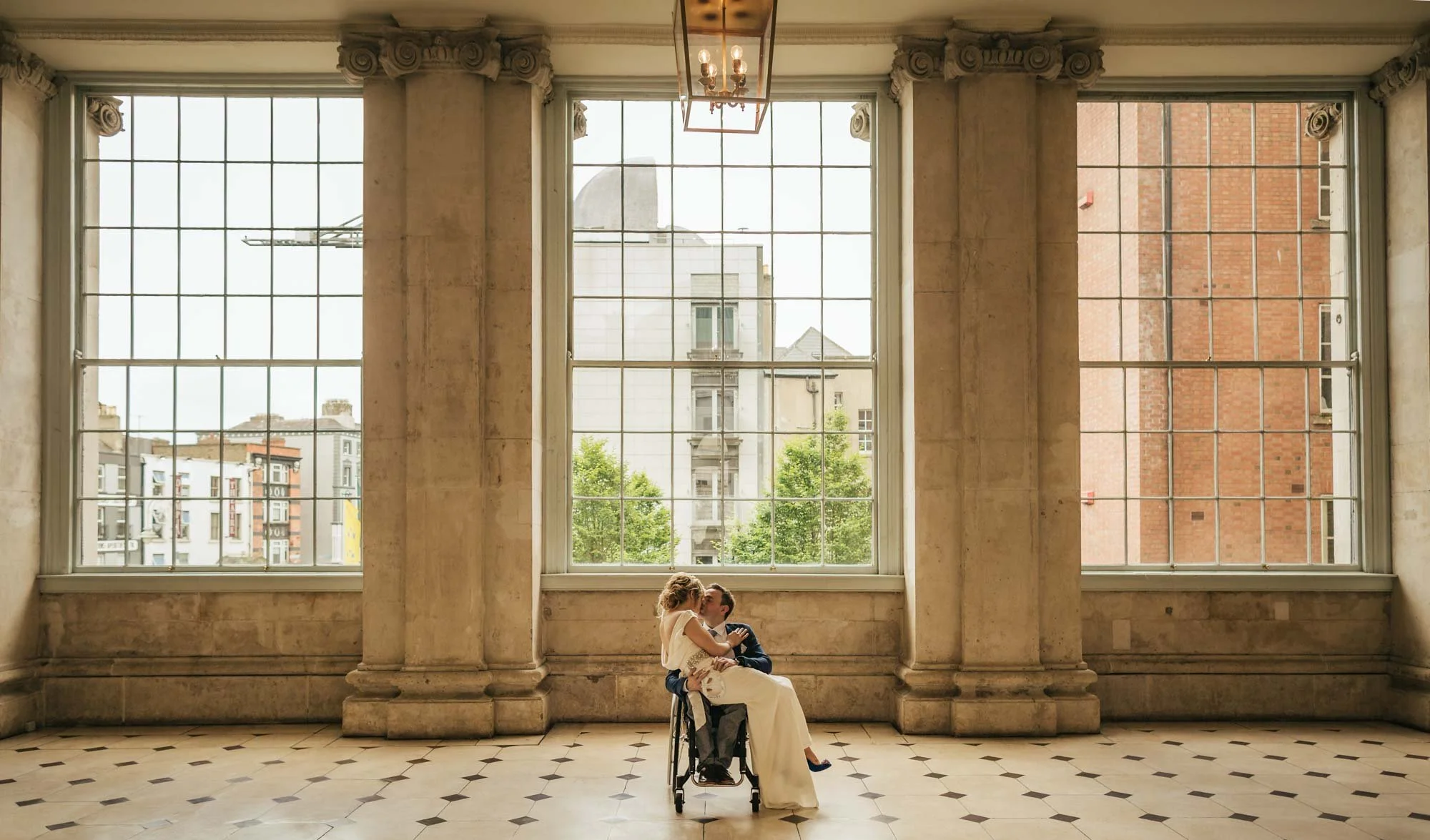 Groom in a wheelchair with his bride on his lap in a classic portrait at Dublin City Hall by Annie Kheffache