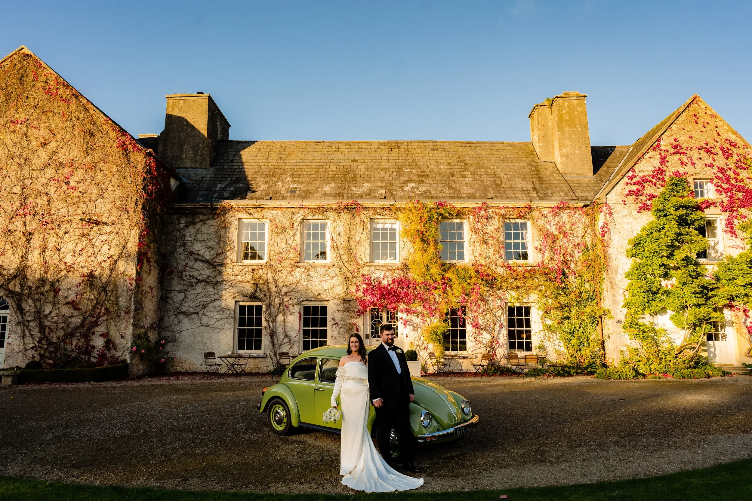 A bride and groom pose in great light in front of the vintage beetle at the front of cloughjordan house wedding venue