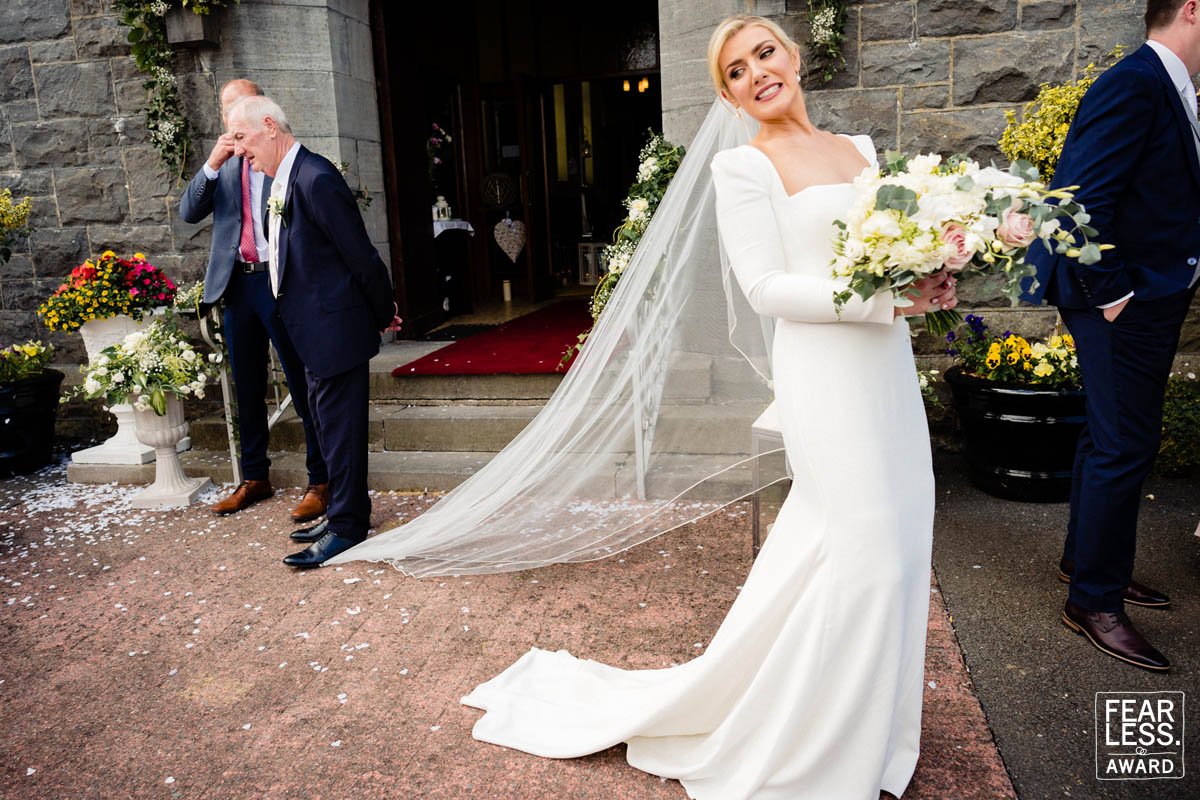 Award winning documentary wedding photography image of the father of the bride standing on the bride's veil outside Dublin wedding ceremony