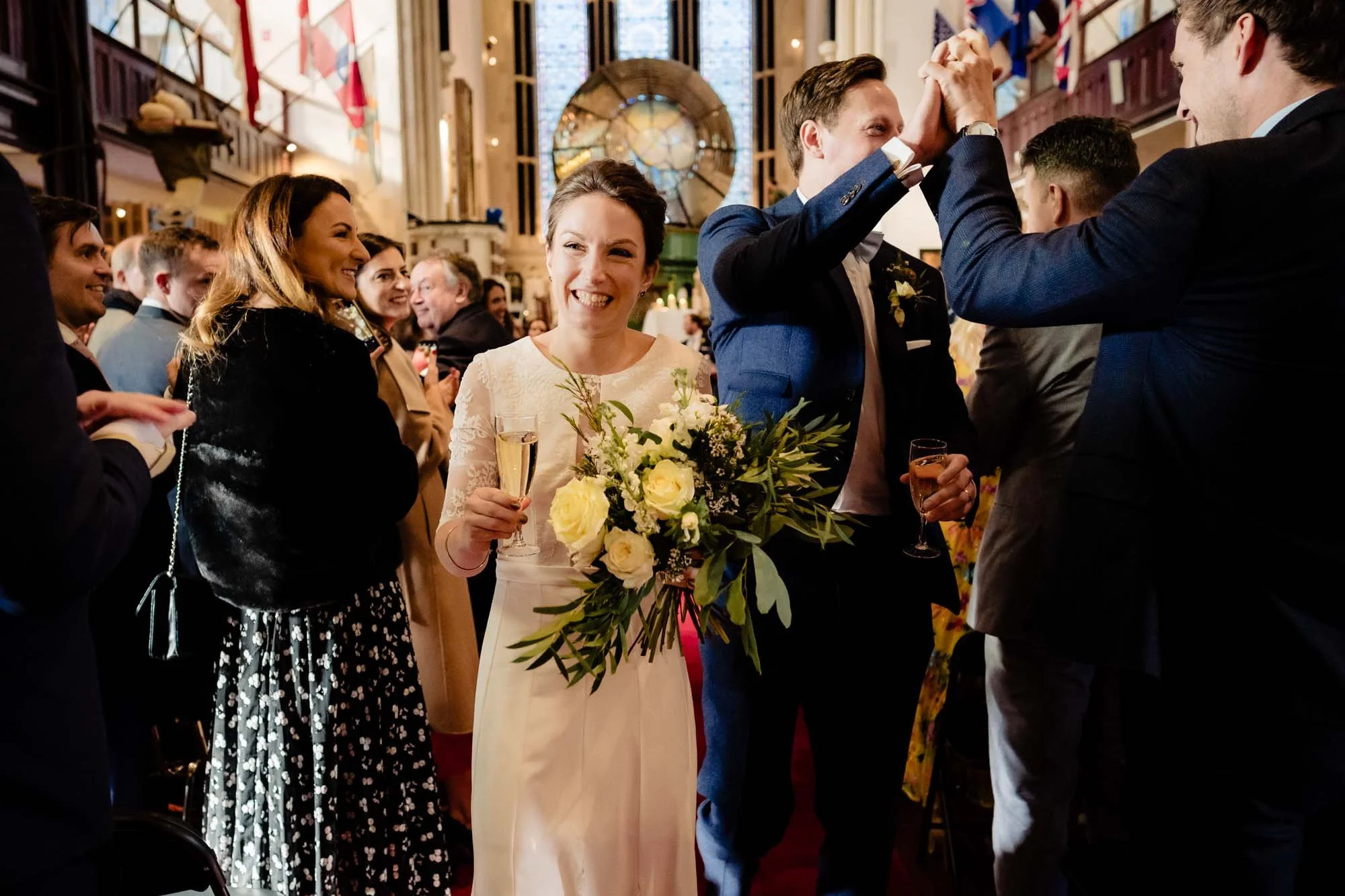 The bride holds champagne and the groom hi-fives guests as they leave their wedding ceremony at the Maritime Museum Dun Laoghaire