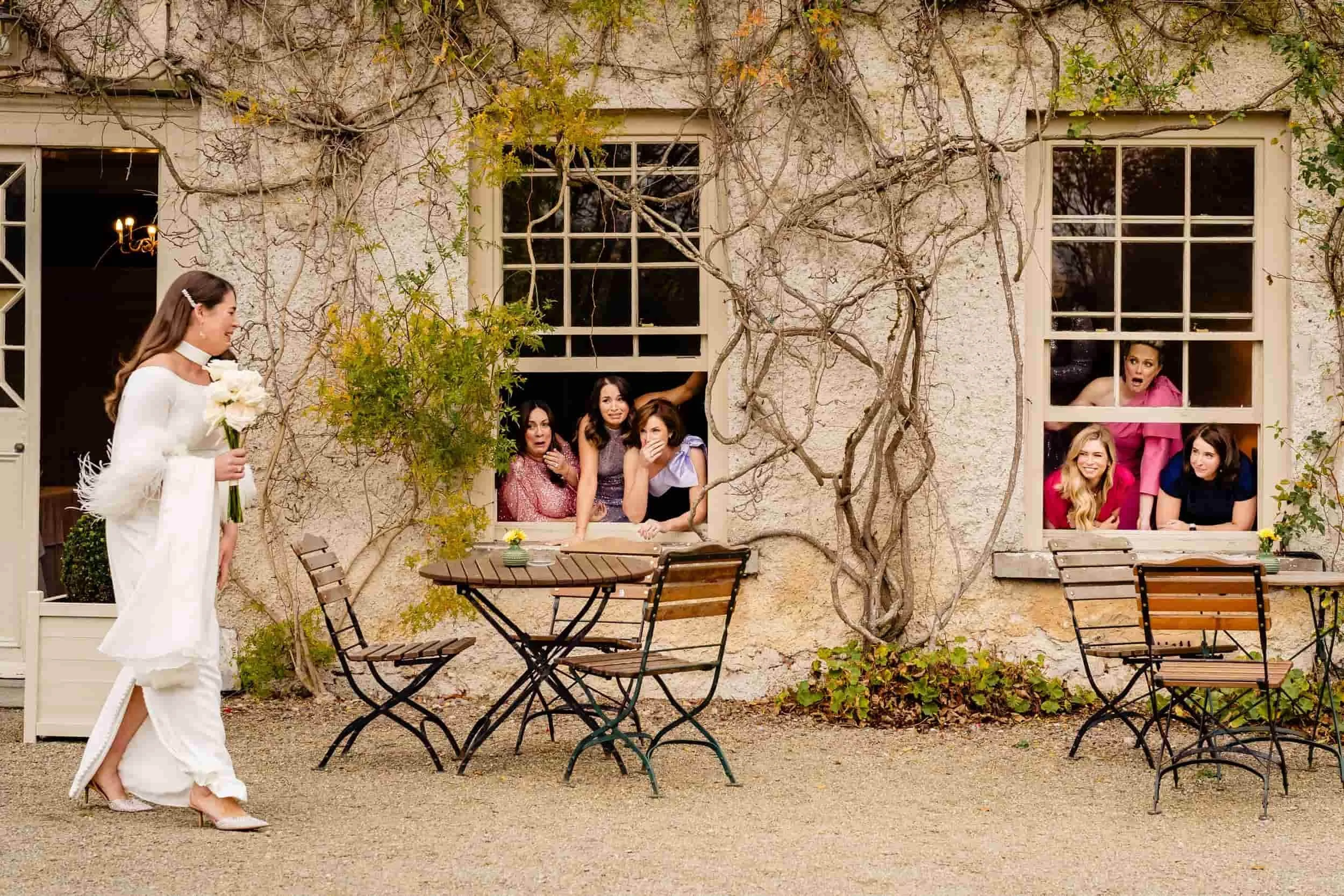 award winning candid wedding photo of bride walkign to first look with bridemaids looking out the window at her