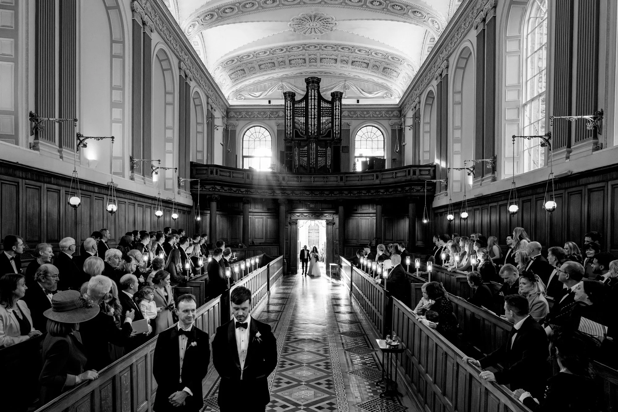 A documentary style wedding photograph of the entrance of the bride at a winter wedding in Trinity College Dublin taken by a Dublin wedding photographer