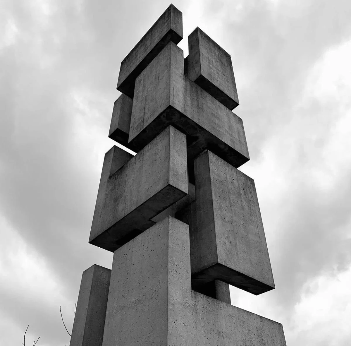 Black and white photograph of a modern abstract concrete sculpture with stacked rectangular blocks against a cloudy sky.