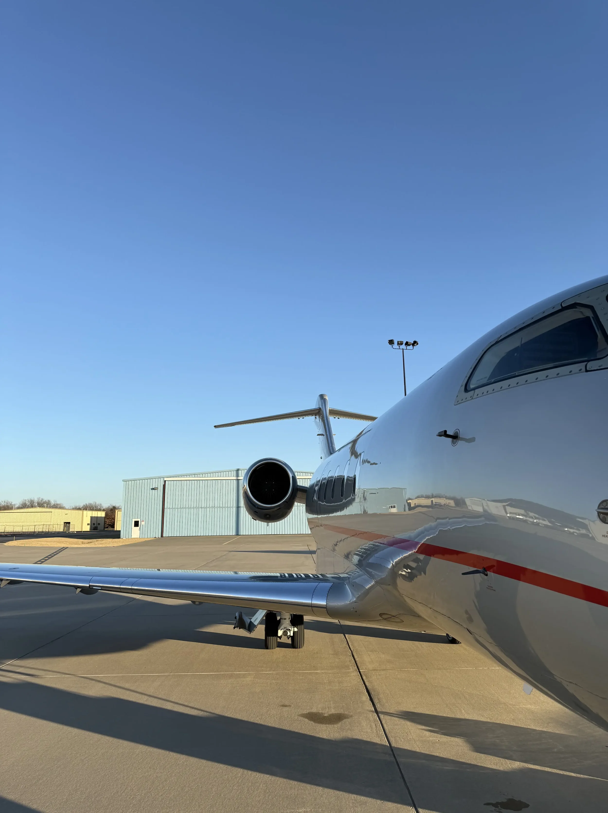 Close-up of a private jet aircraft on the tarmac, showing part of the fuselage, wing, and engine under a clear blue sky showcasing an exterior wash results