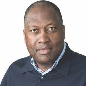 A man wearing a navy blue polo shirt and a light blue collared shirt underneath, looking directly at the camera with a neutral expression.