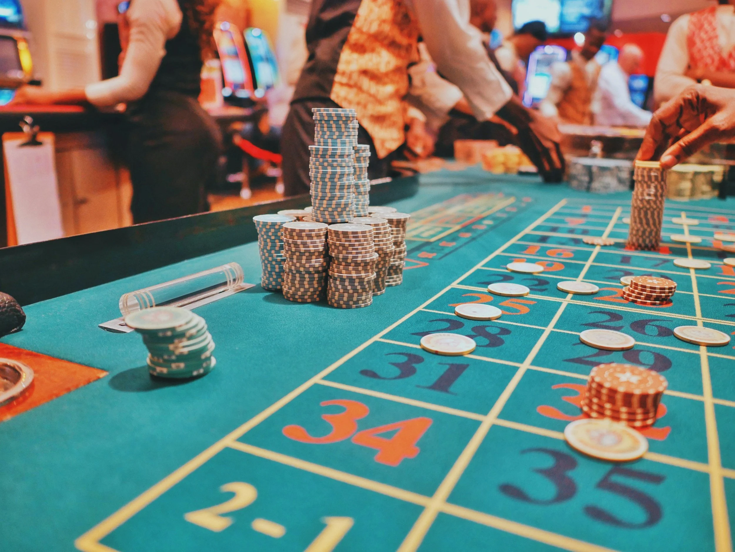 Casino craps table with stacked poker chips in the center and people playing in the background.