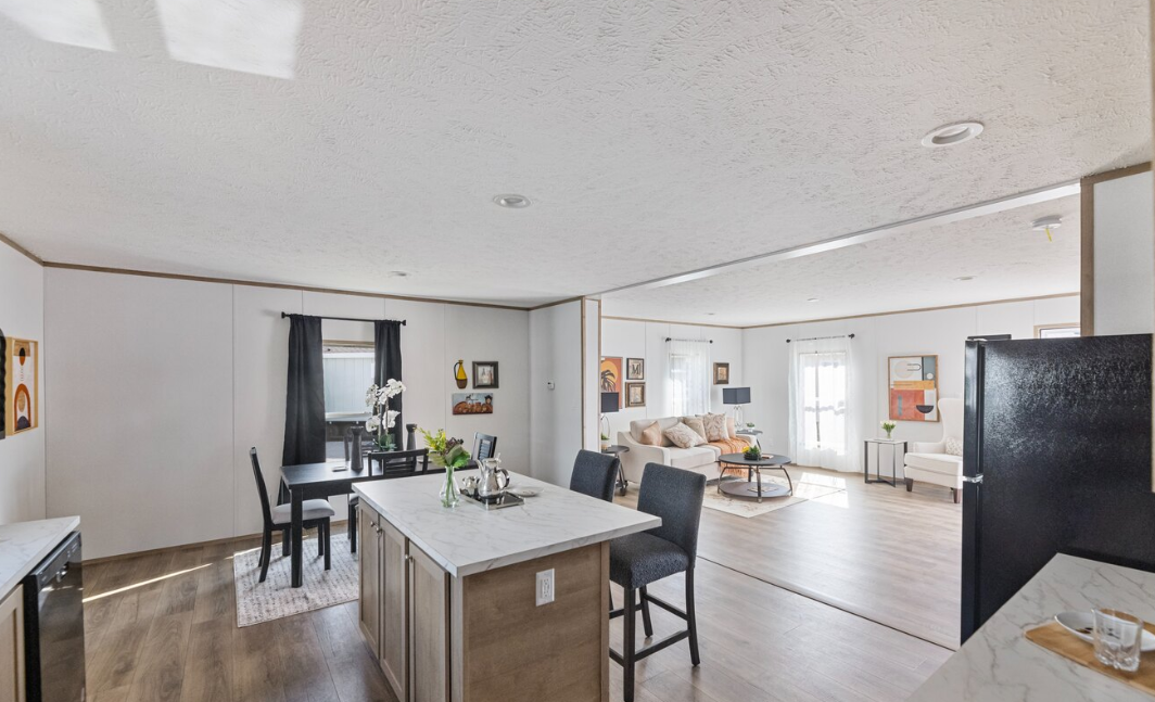 Open-concept kitchen and living room with modern decor, white walls, wooden floors, black curtains on windows, and various wall art.