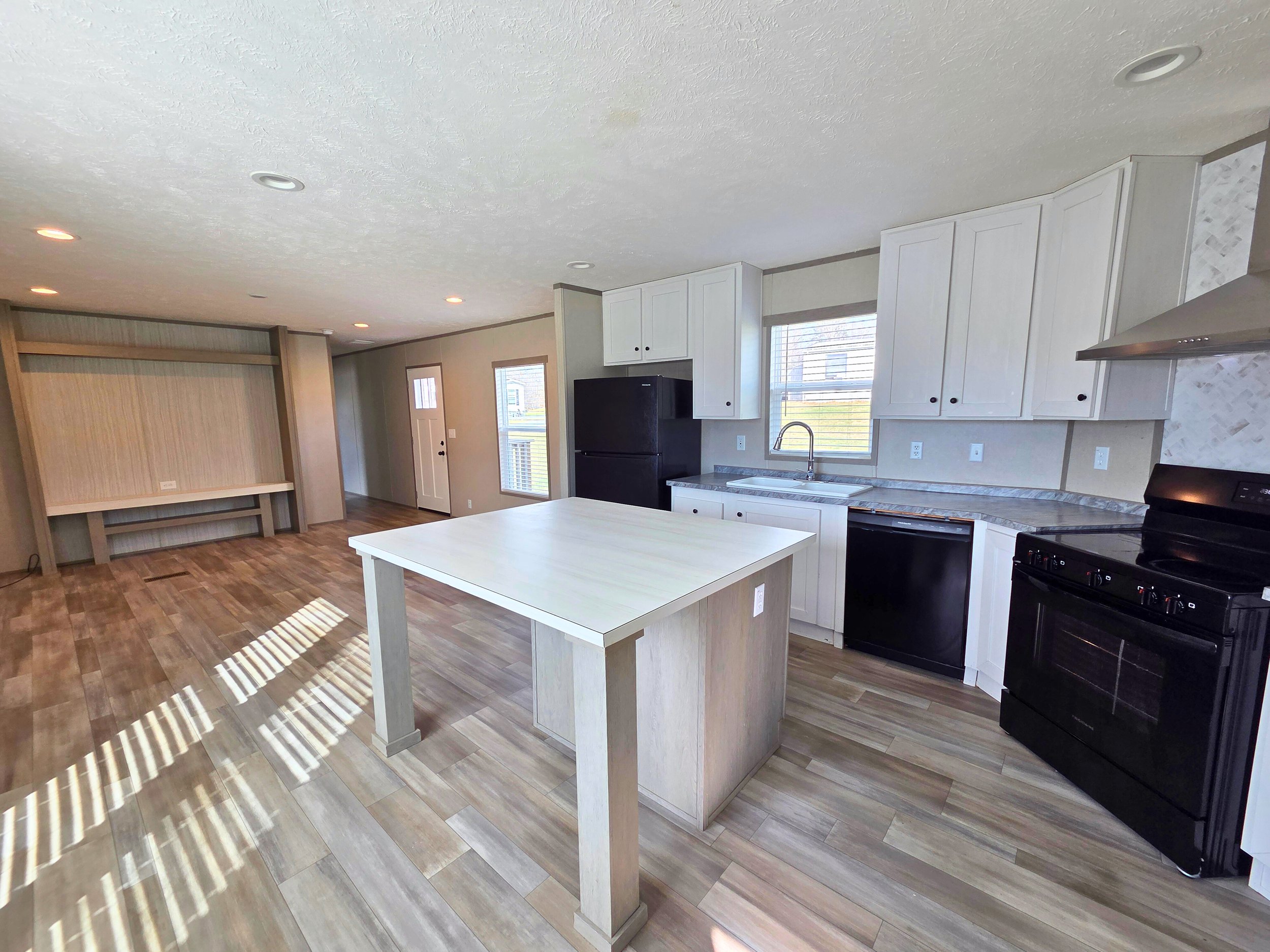 A white manufactured home with black shutters and a small front porch, set on a grassy lawn under a partly cloudy sky.