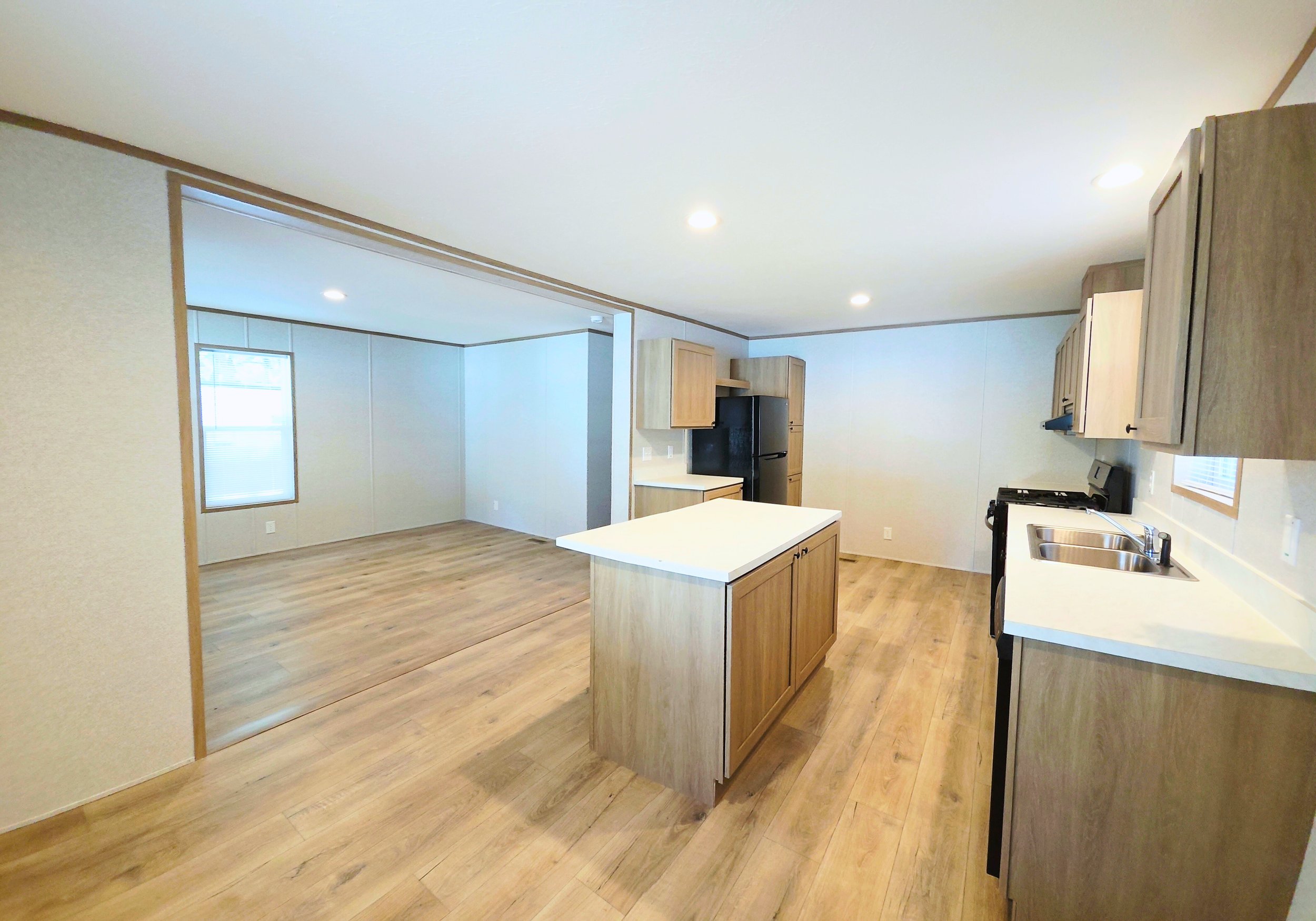Open-concept kitchen and living area with wood flooring, light wood cabinets, a kitchen island, and black appliances.