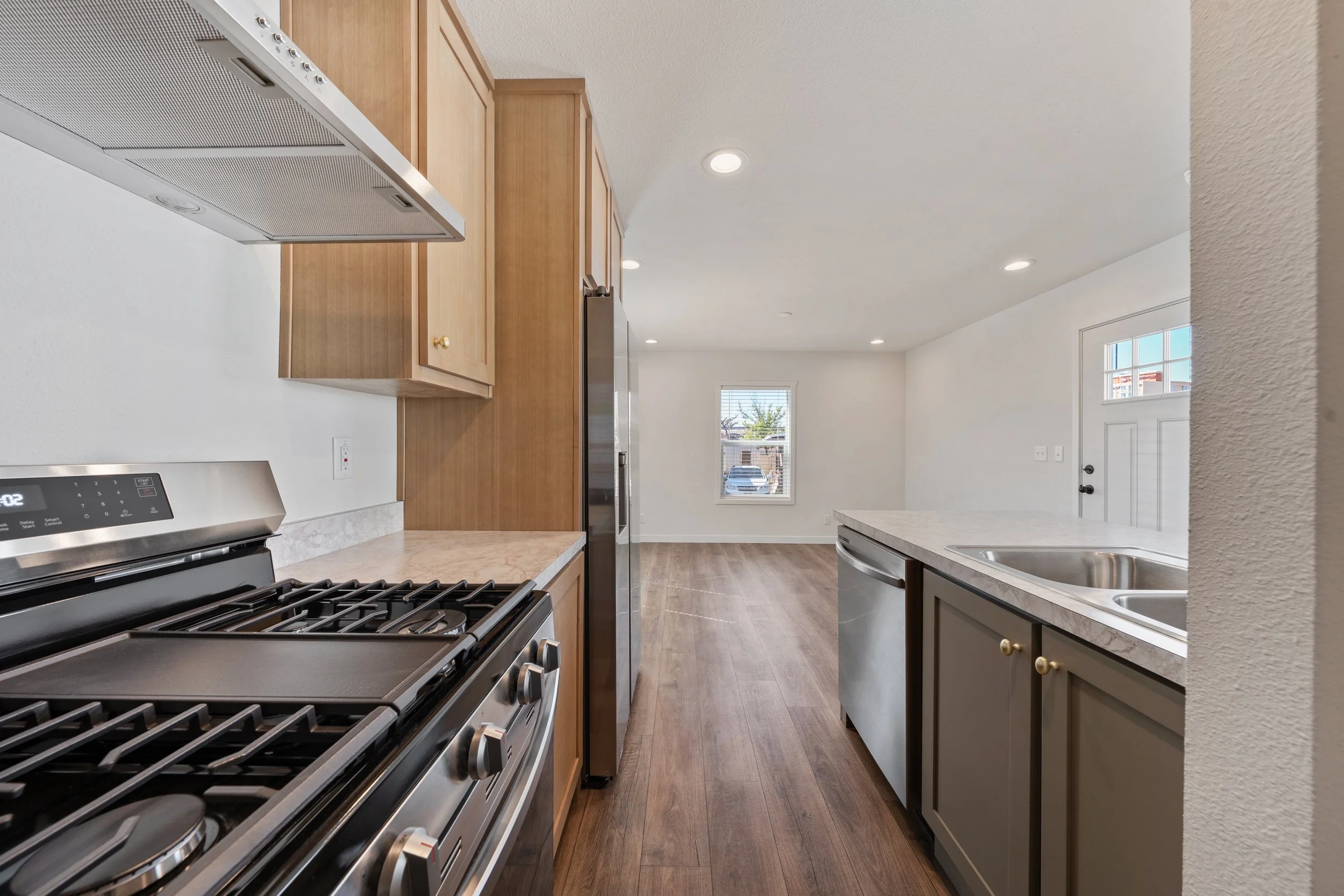 Kitchen with wooden cabinets, a stainless steel stove, refrigerator, and dishwasher, white walls, and hardwood flooring.