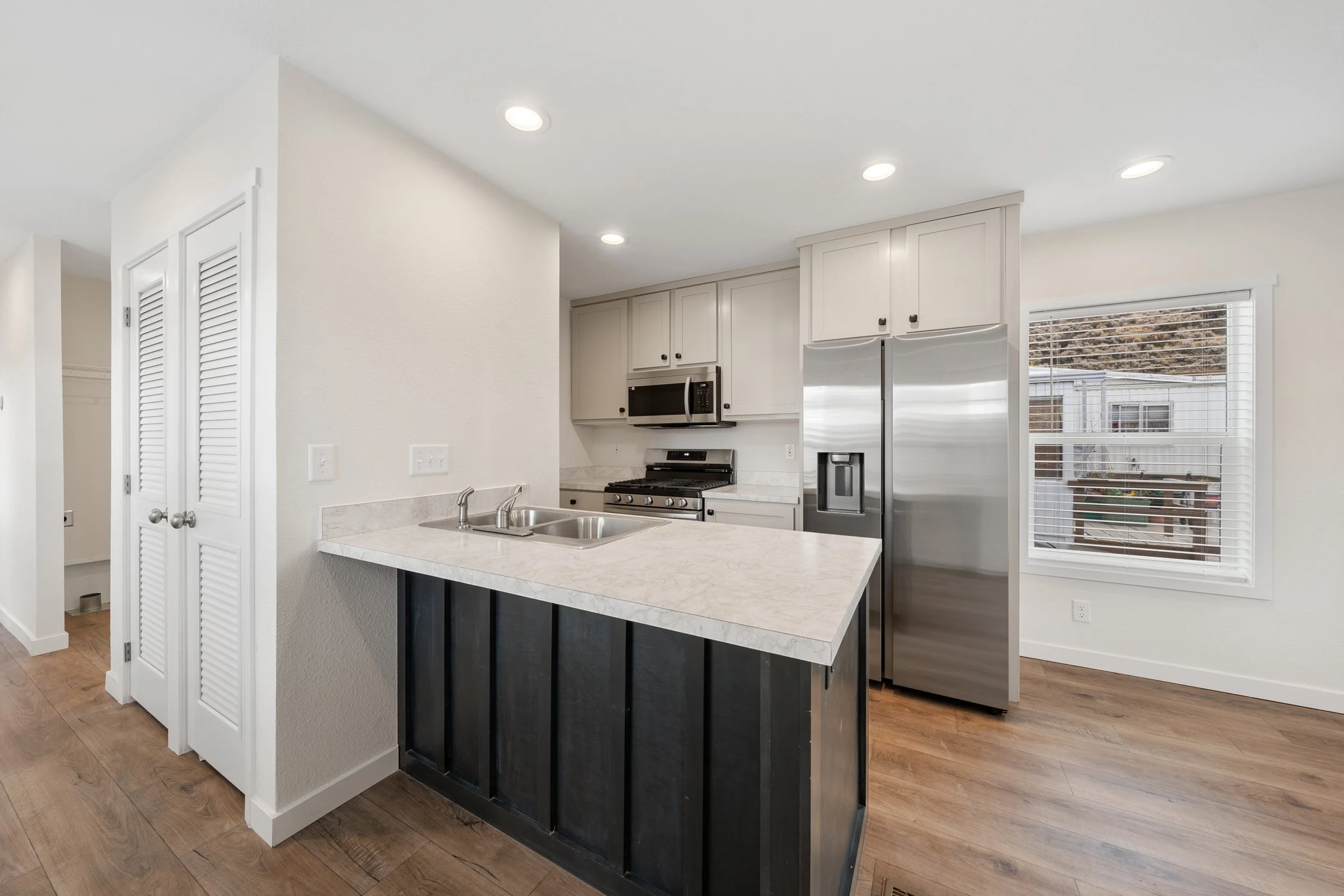 Modern kitchen with white cabinets, stainless steel appliances, a marble countertop island, and a window showing outdoor view with neighboring buildings.