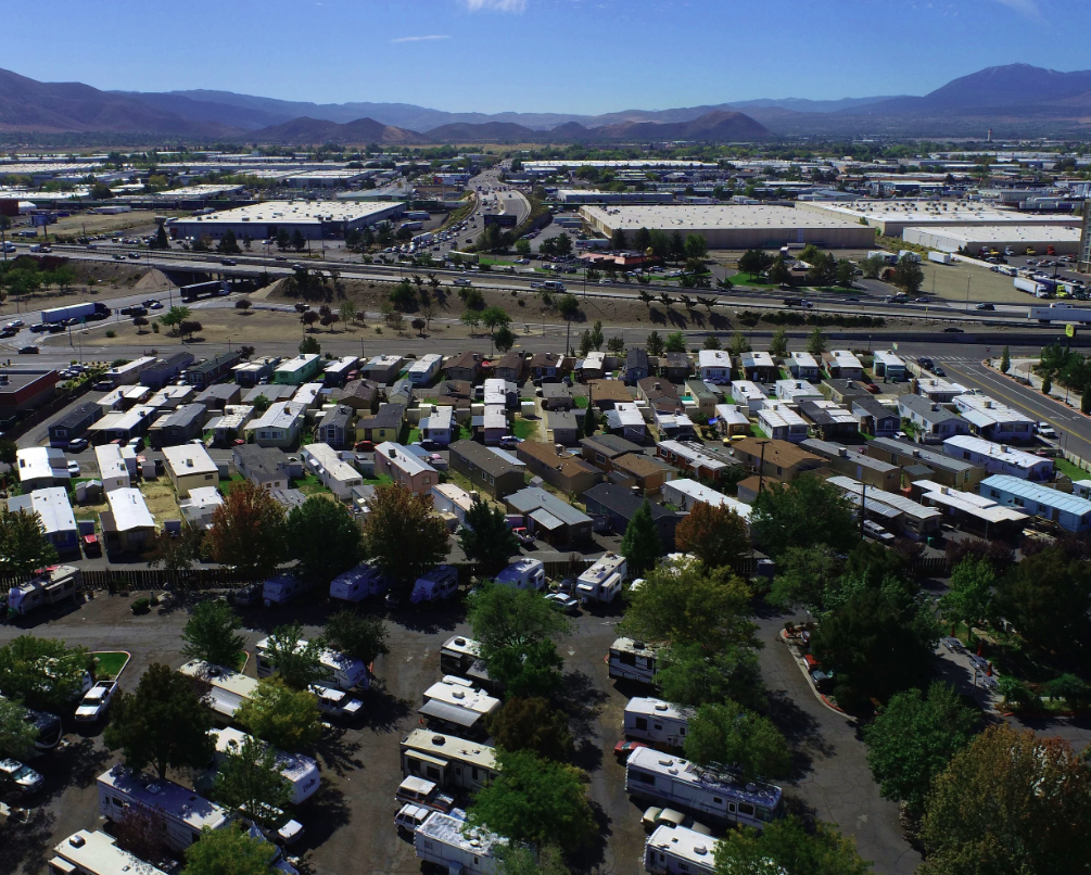 Aerial view of a landscape including a residential area with mobile homes, a commercial industrial complex, highways, and mountainous terrain in the distance.