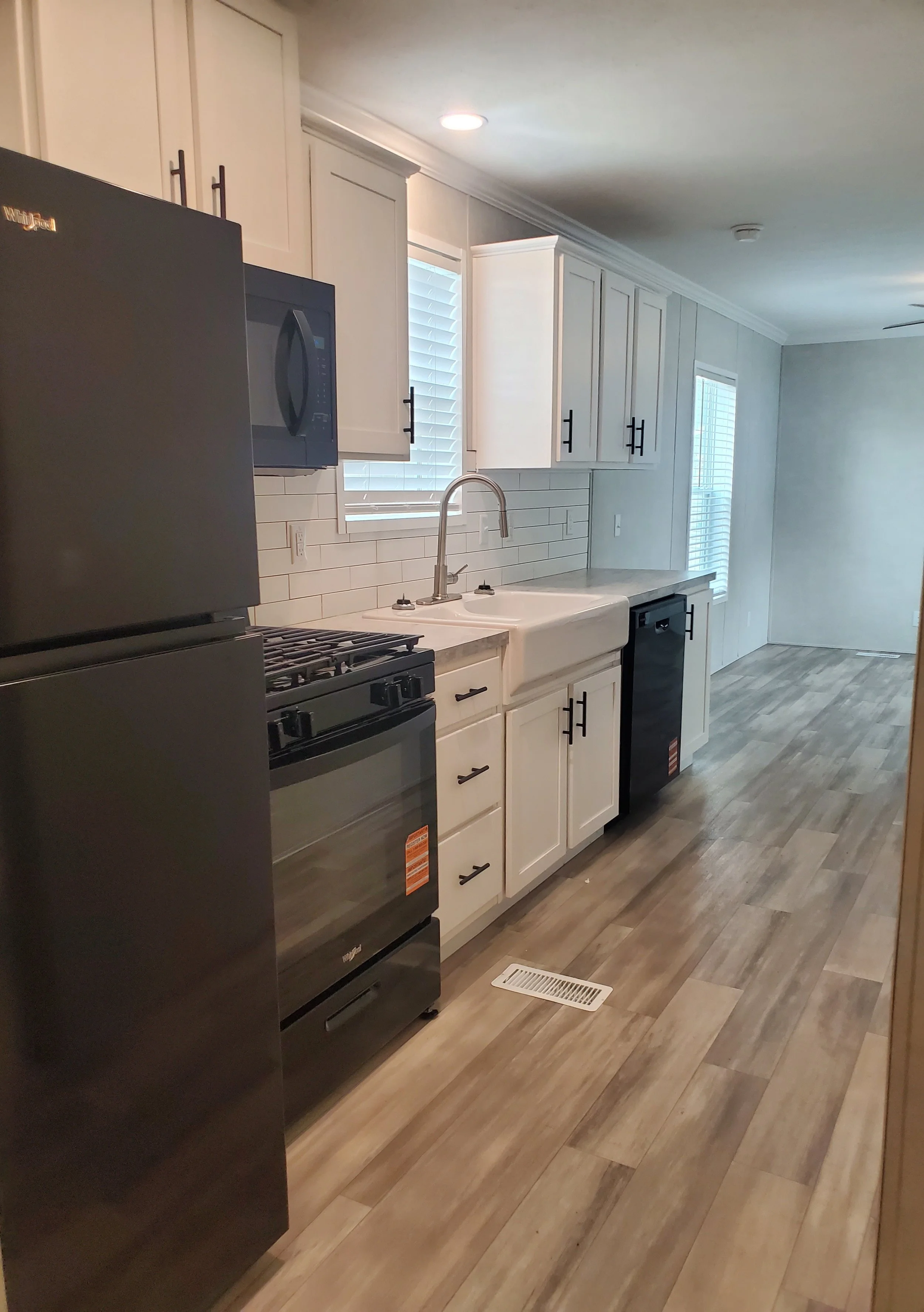 Empty kitchen with light wood cabinets, black refrigerator, granite countertops, and a breakfast bar. Decor includes small vases with orange flowers, and a ceiling fan with light.