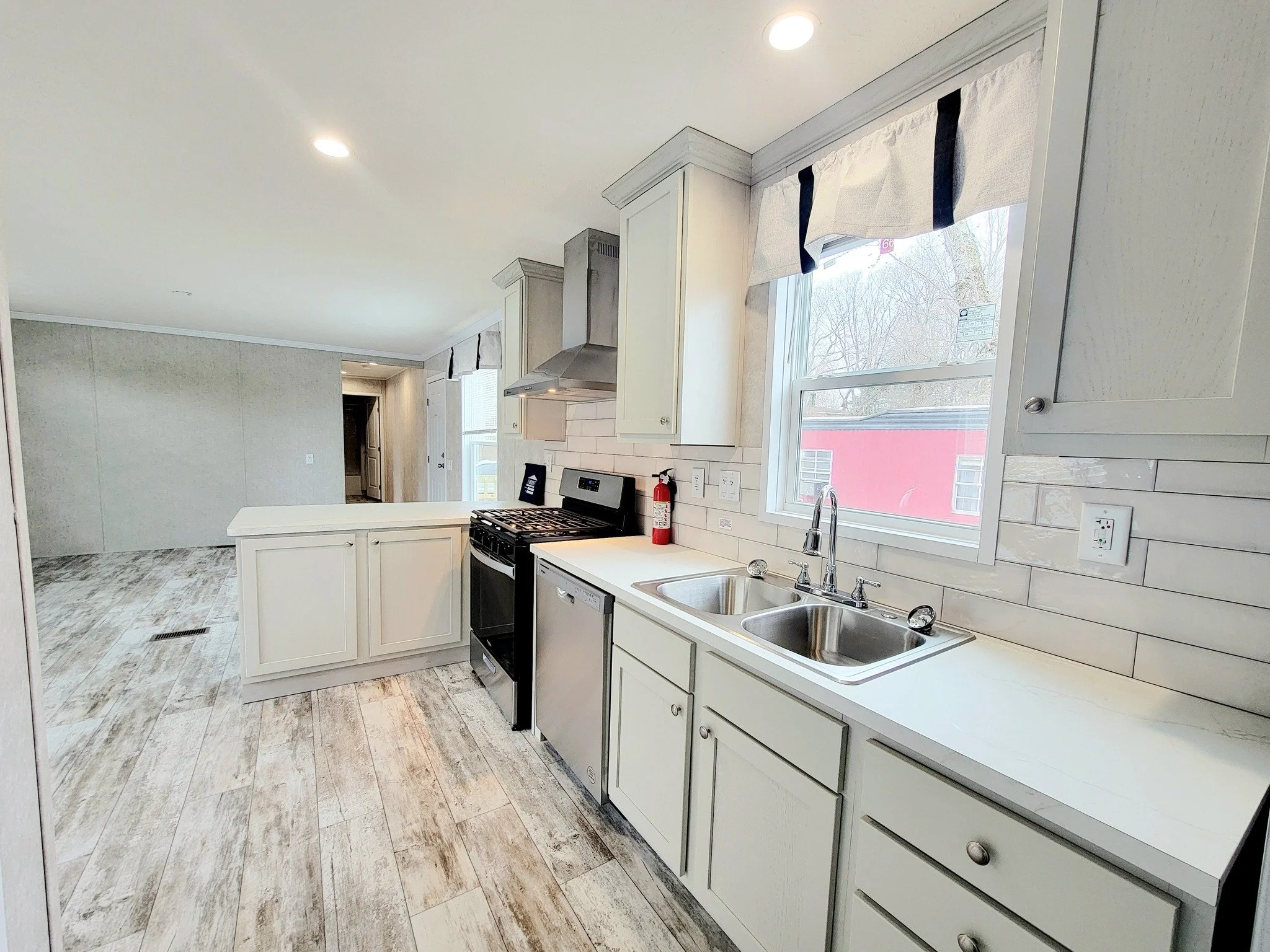 Kitchen with white cabinets, a stainless steel stove, a dishwasher, double sink, window, and beige tile backsplash.