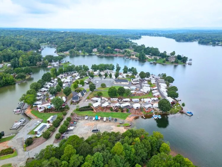 Aerial view of a lakeside residential community with houses, trees, boats, and water.