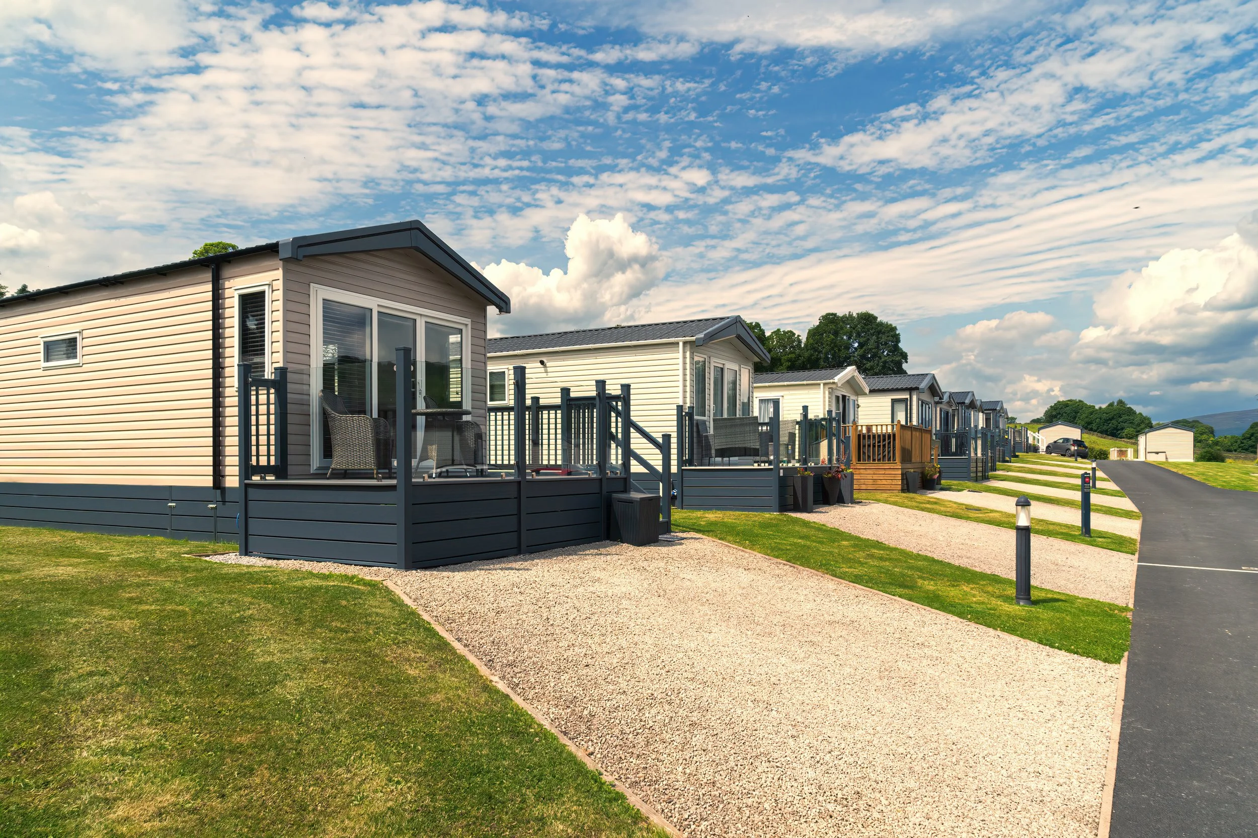 Row of modern mobile homes with small decks and landscaped yards under a partly cloudy sky