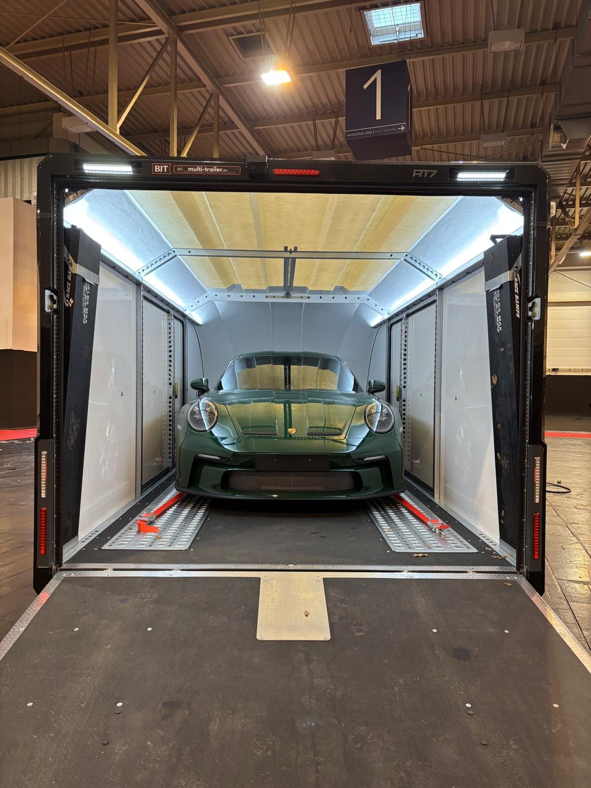 Green Porsche 911 ST 2024 inside a brian james trailer cartransporter  with lighting, at an exhibition or storage facility at Messe Essen.