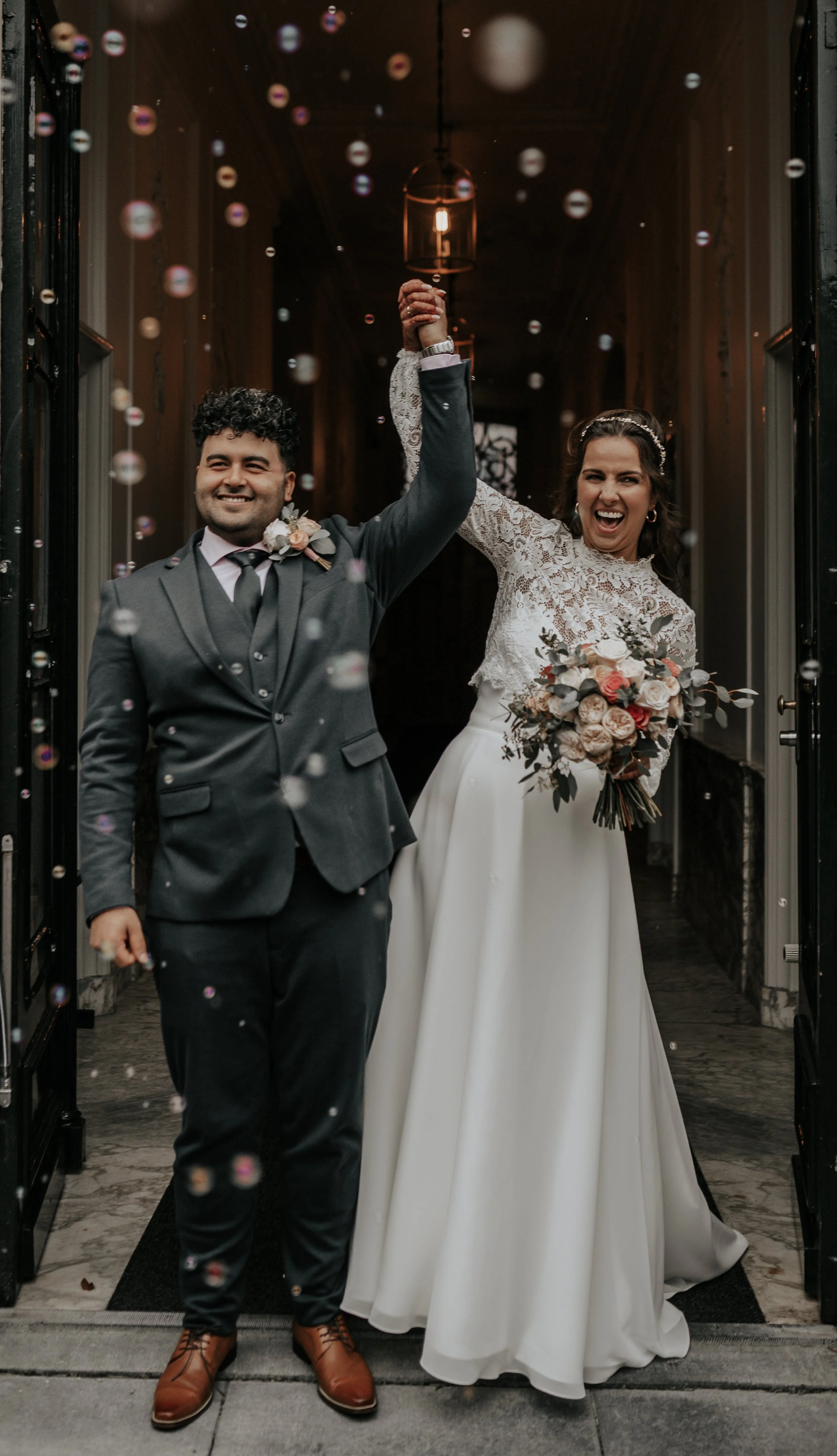 Een nieuw getrouwd paar dat samen aankomt, de bruid houdt een boeket bloemen vast en de bruidegom draagt een grijs pak, ze vieren hun huwelijk onder confetti.