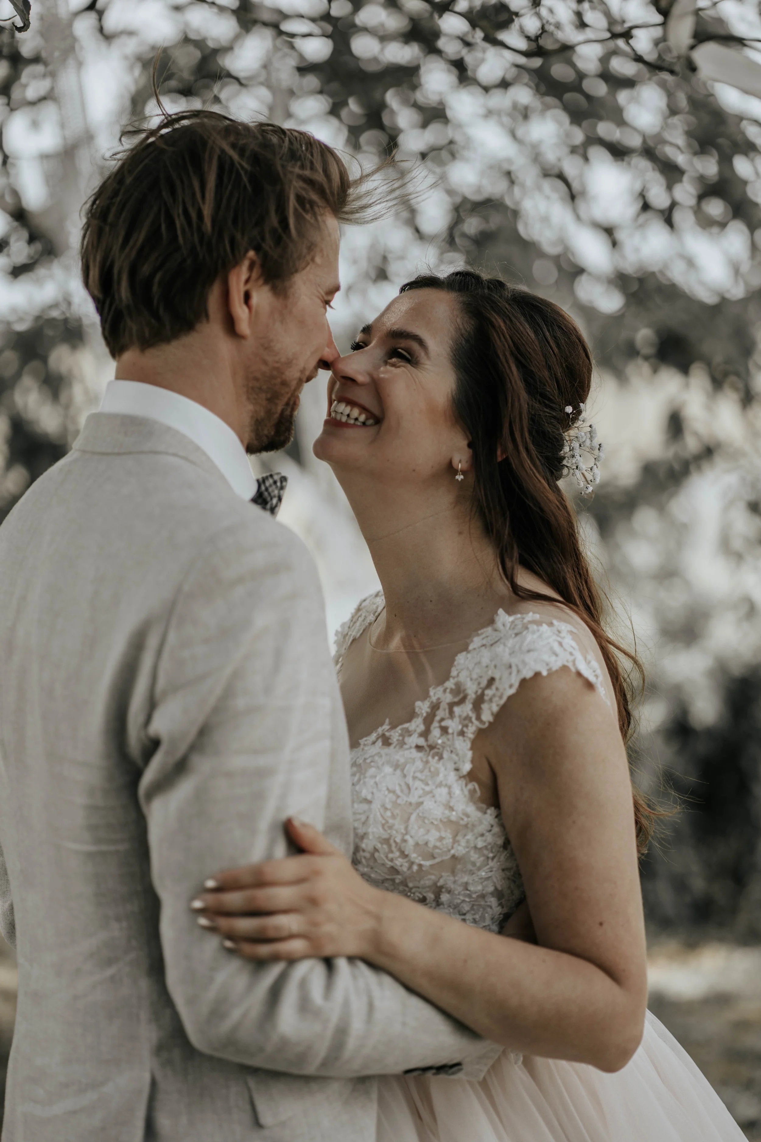 Een bruid en bruidegom die gelukkig lachen en elkaar bijna kussen, buiten onder een boom.