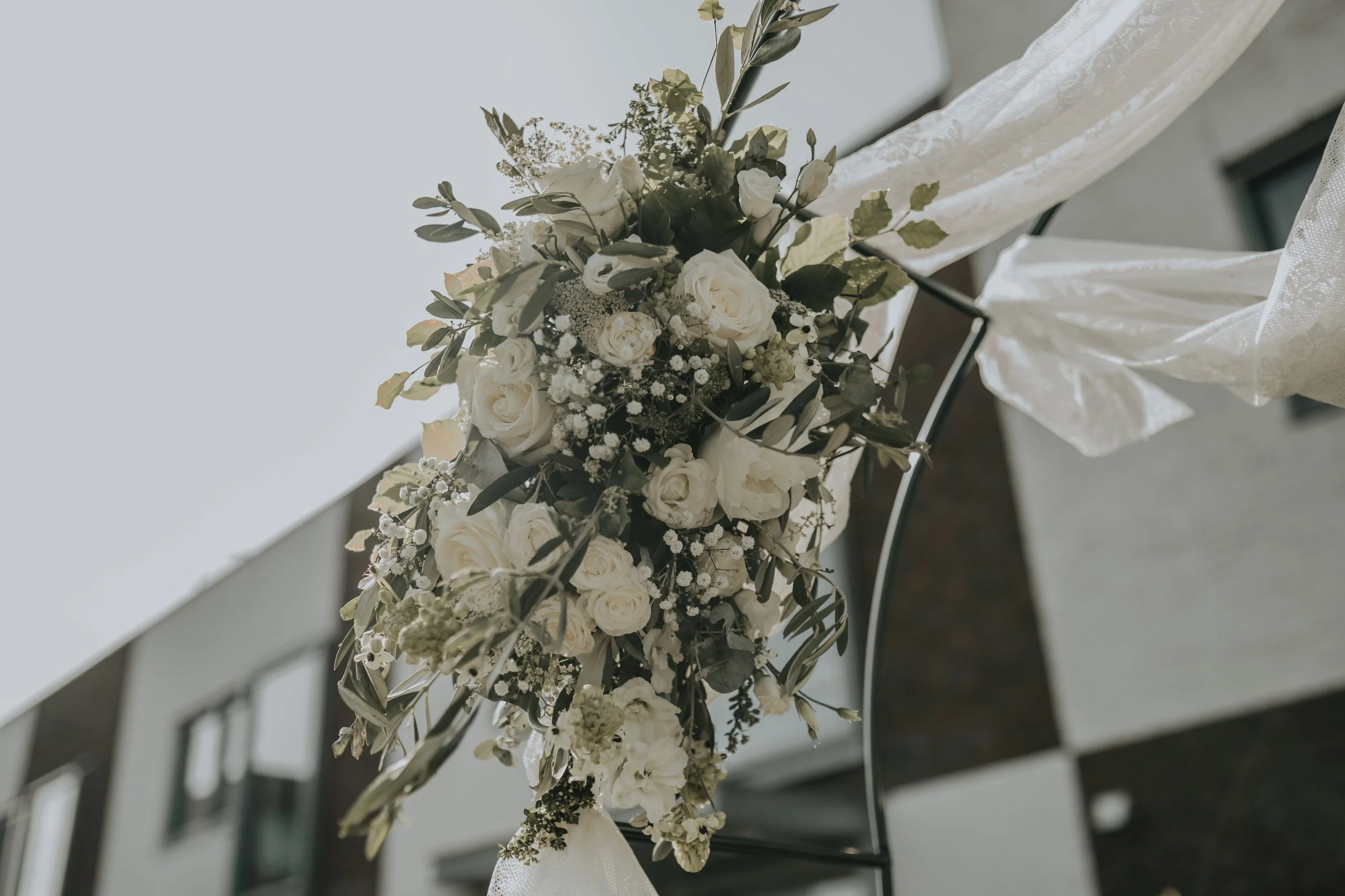 Witte bloemendecoratie met rozen en groene bladeren aan een metalen frame naast een muur