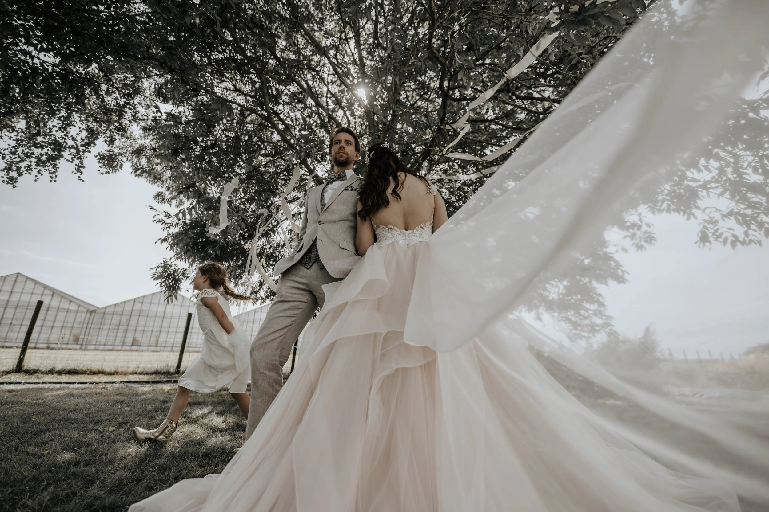 Bruidsparen en een kind onder een grote boom, buiten, in een landelijk landschap.