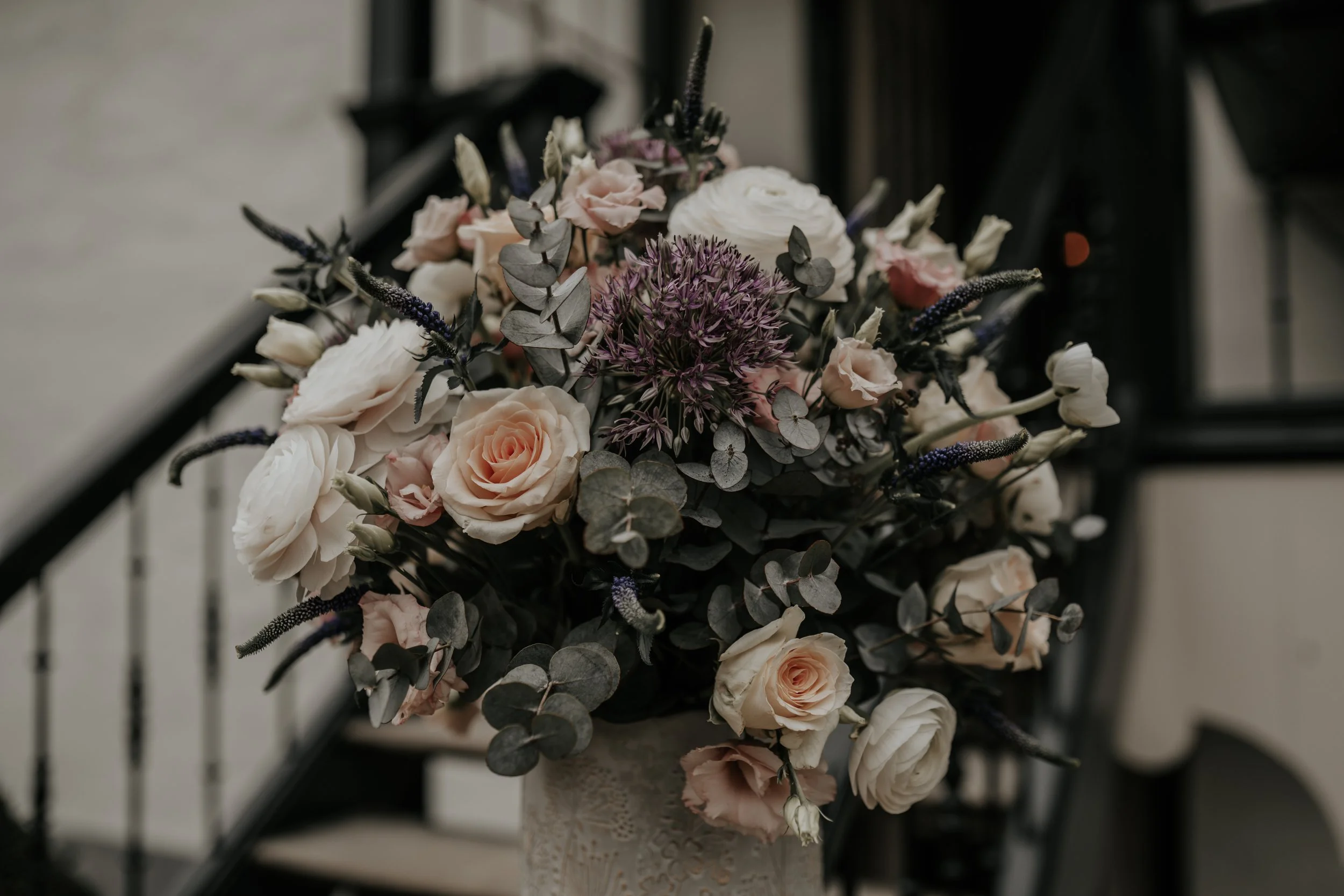 Een bos bloemen in een vaas, met roze en witte rozen, eucalyptusbladeren en andere bloemensoorten, geplaatst op een trap.