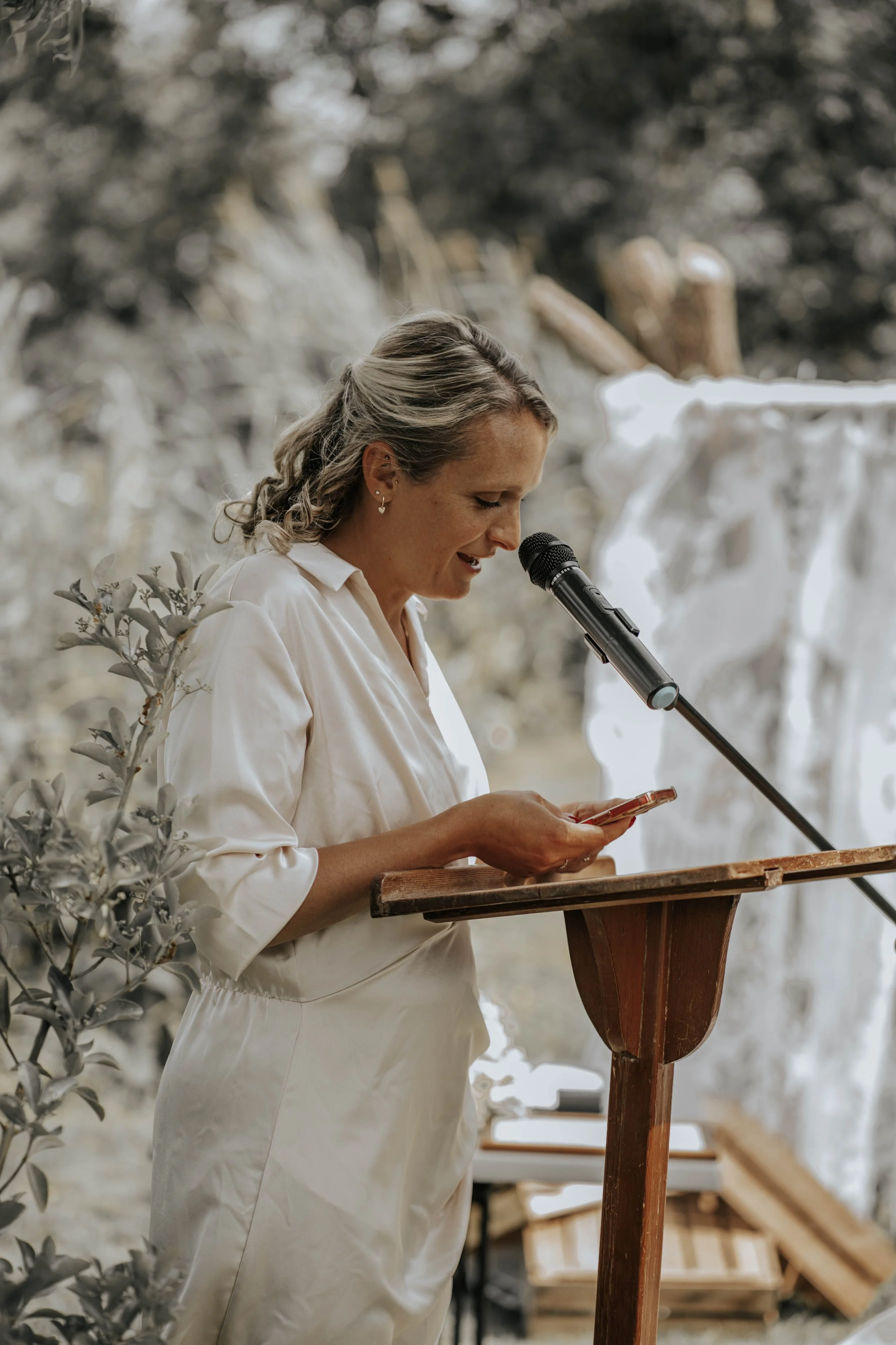 Vrouw leest een speech voor tijdens een ceremonie, met een microfoon voor haar en een houten lectuurbord.