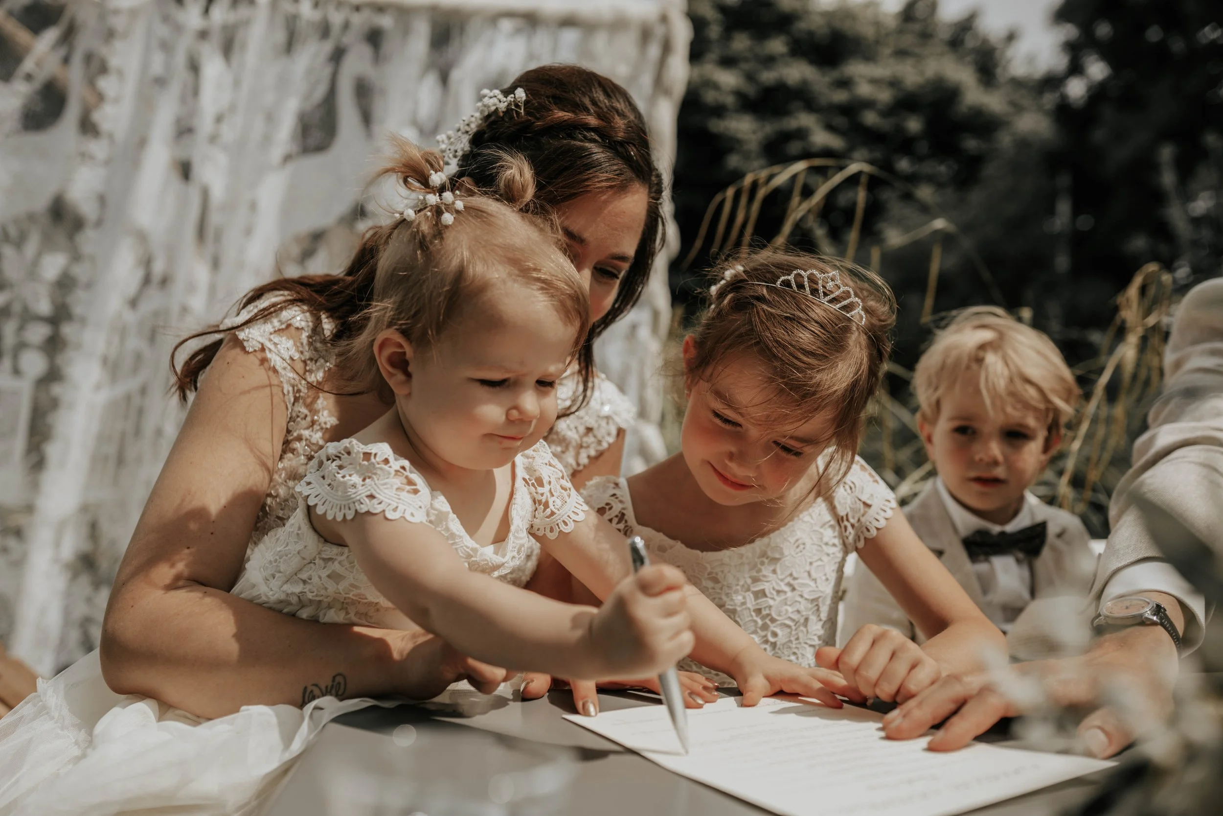 Een bruid die samen met drie jonge kinderen een document ondertekent tijdens een buitenbruiloft.