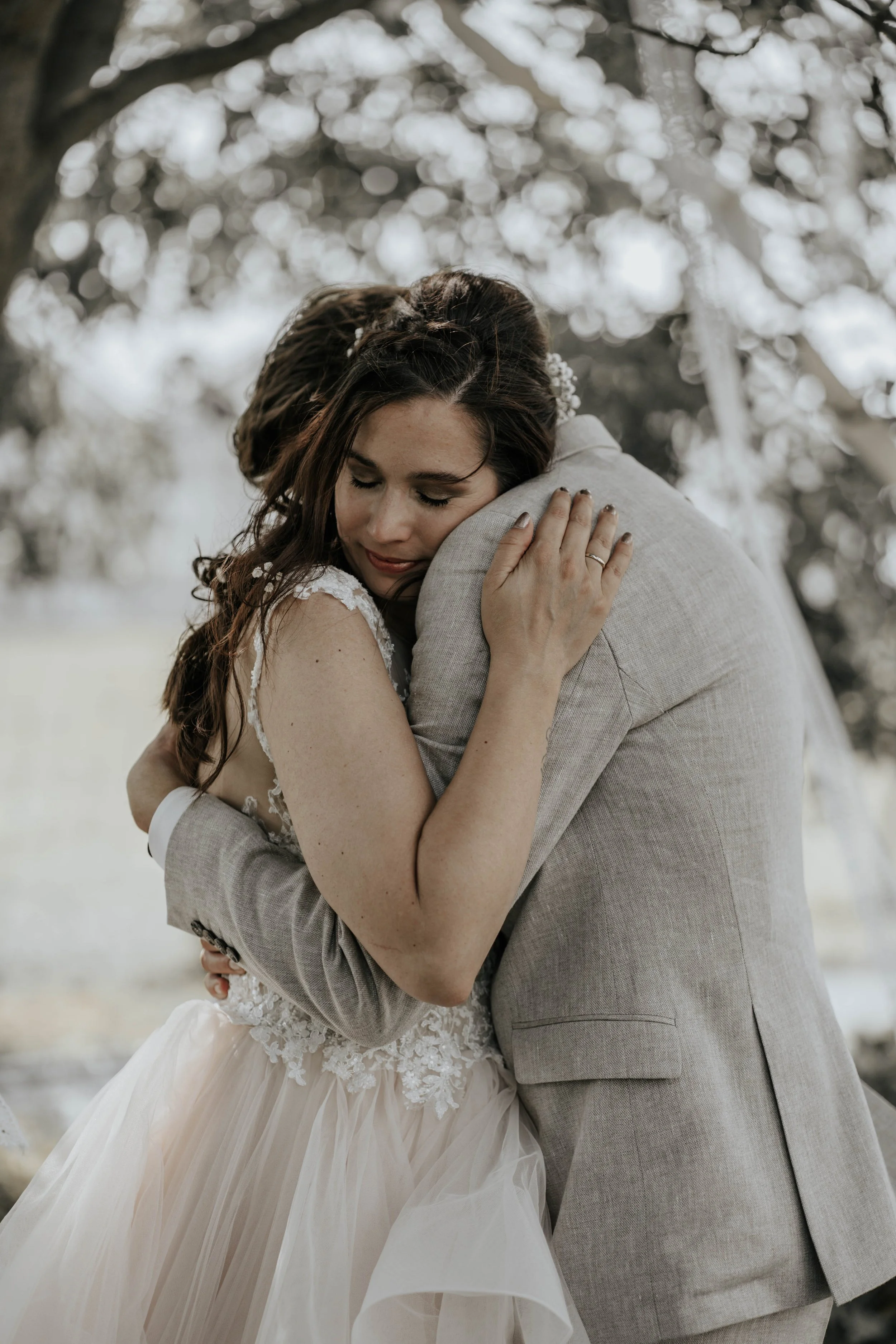 Koppels die elkaar omhelzen, waarschijnlijk op een bruiloft, met een boom en een natuurachtergrond.