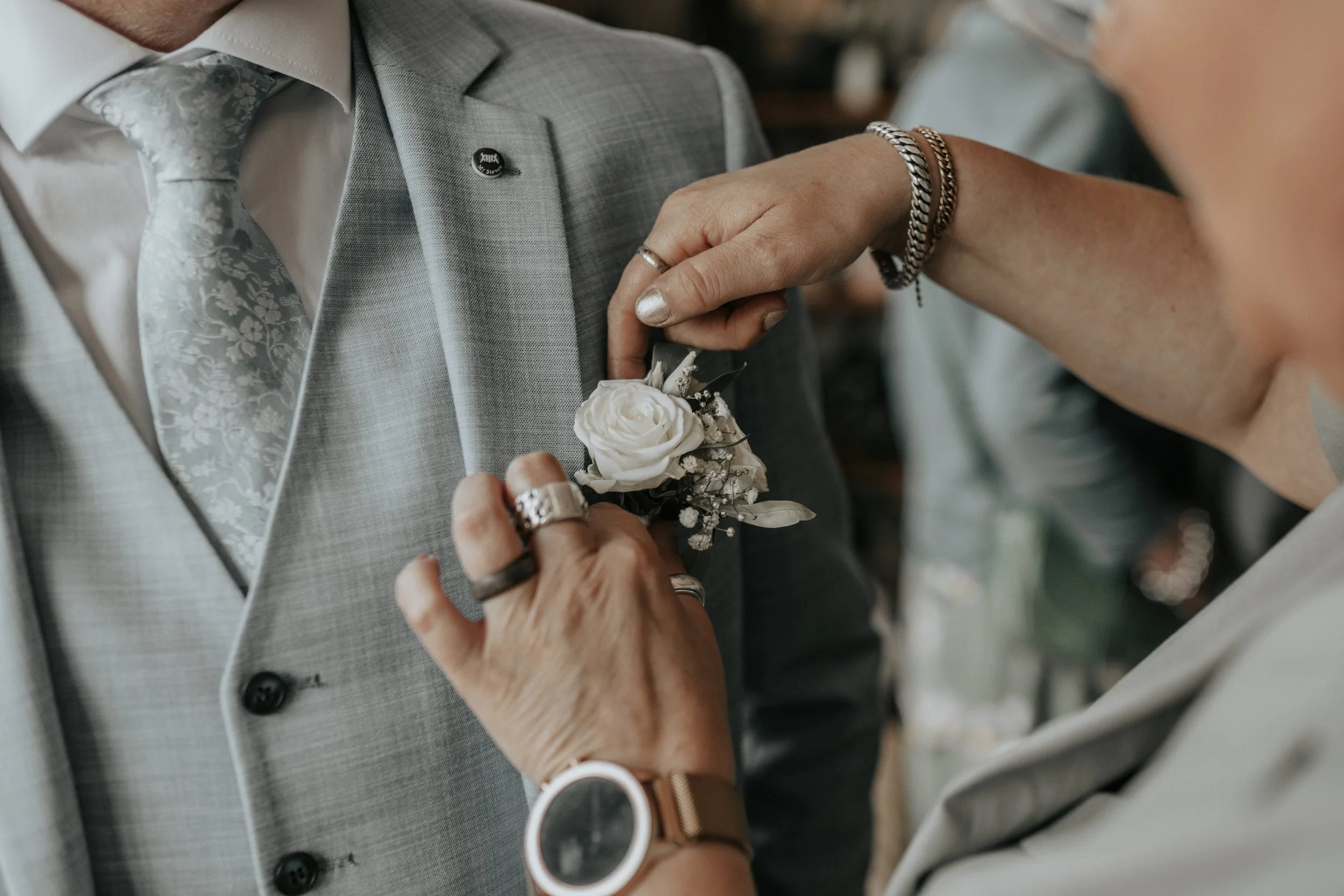 Vrouw bevestigt een bloemhoekje op de jas van een man tijdens een huwelijk of formele gelegenheid.