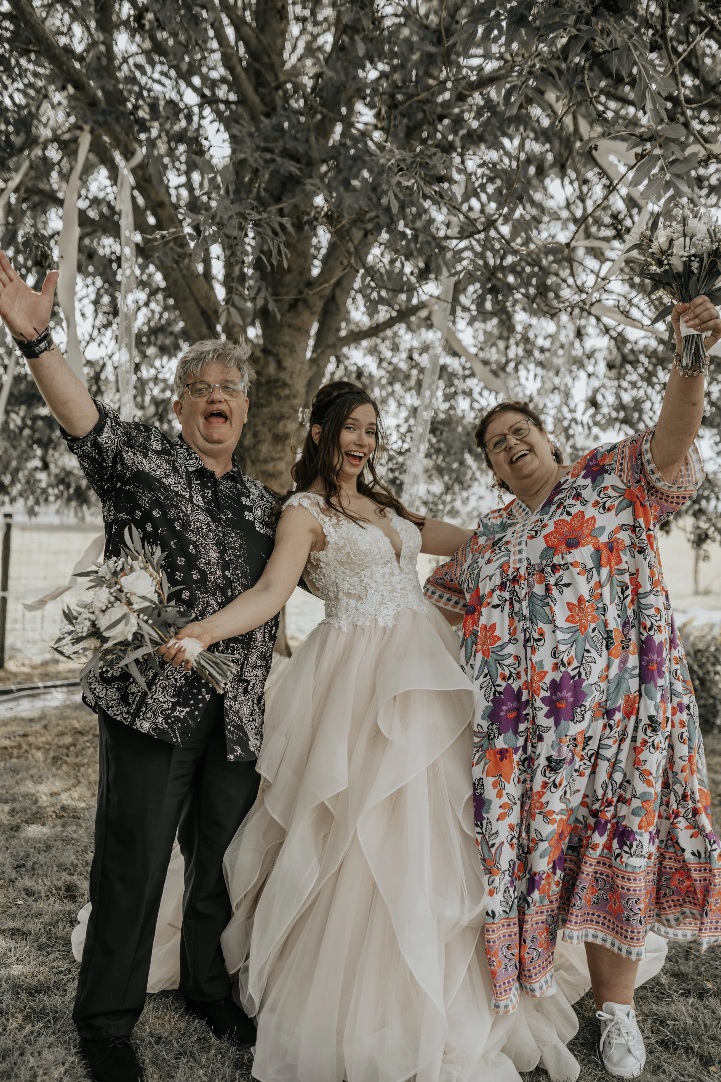 Een huwelijksfeest met een bruid in een witte jurk en twee mensen die vieren onder een boom.