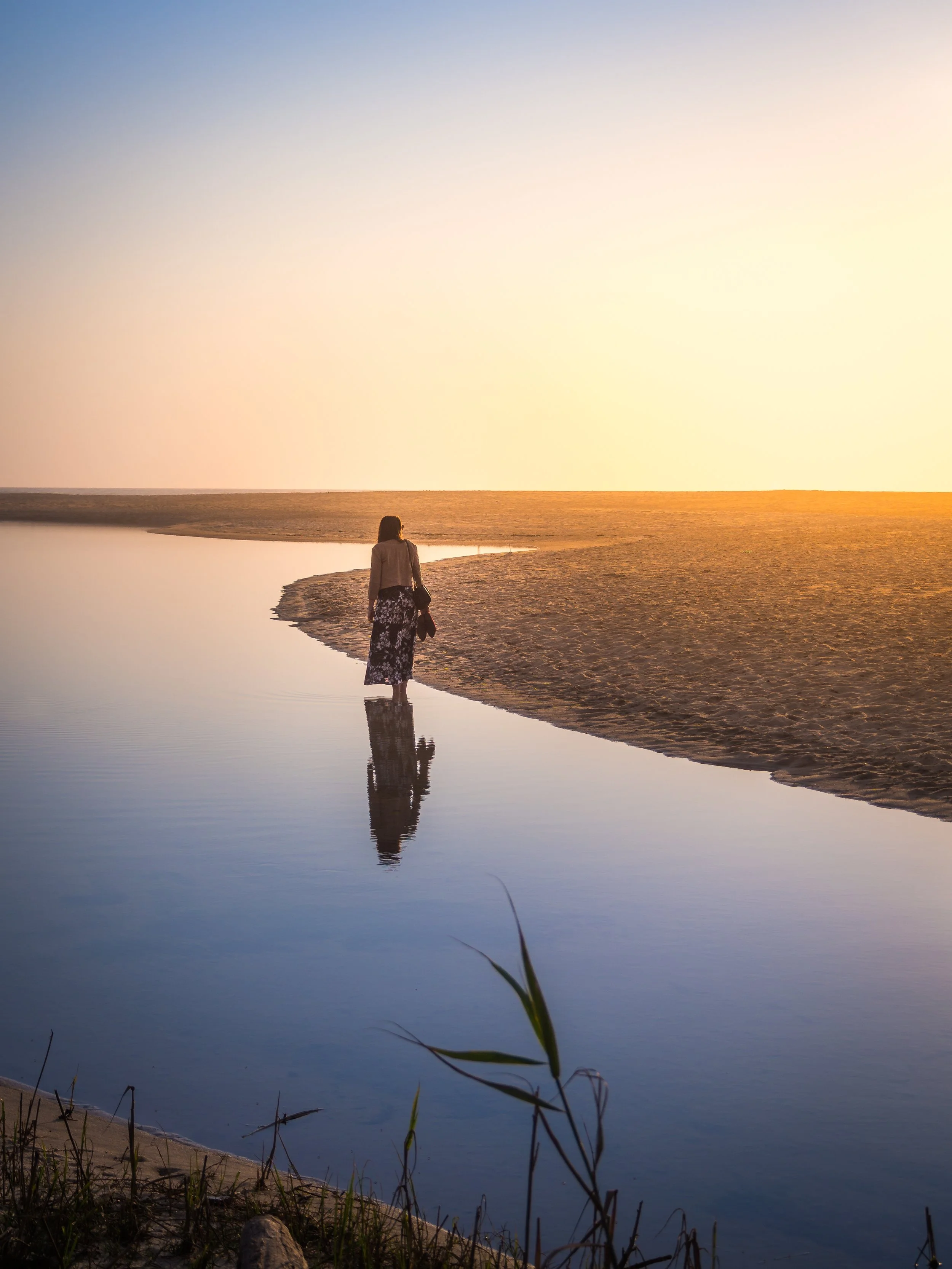 Une femme marche le long de la rive d'une rivière lors du coucher du soleil, avec une réflexion dans l'eau
