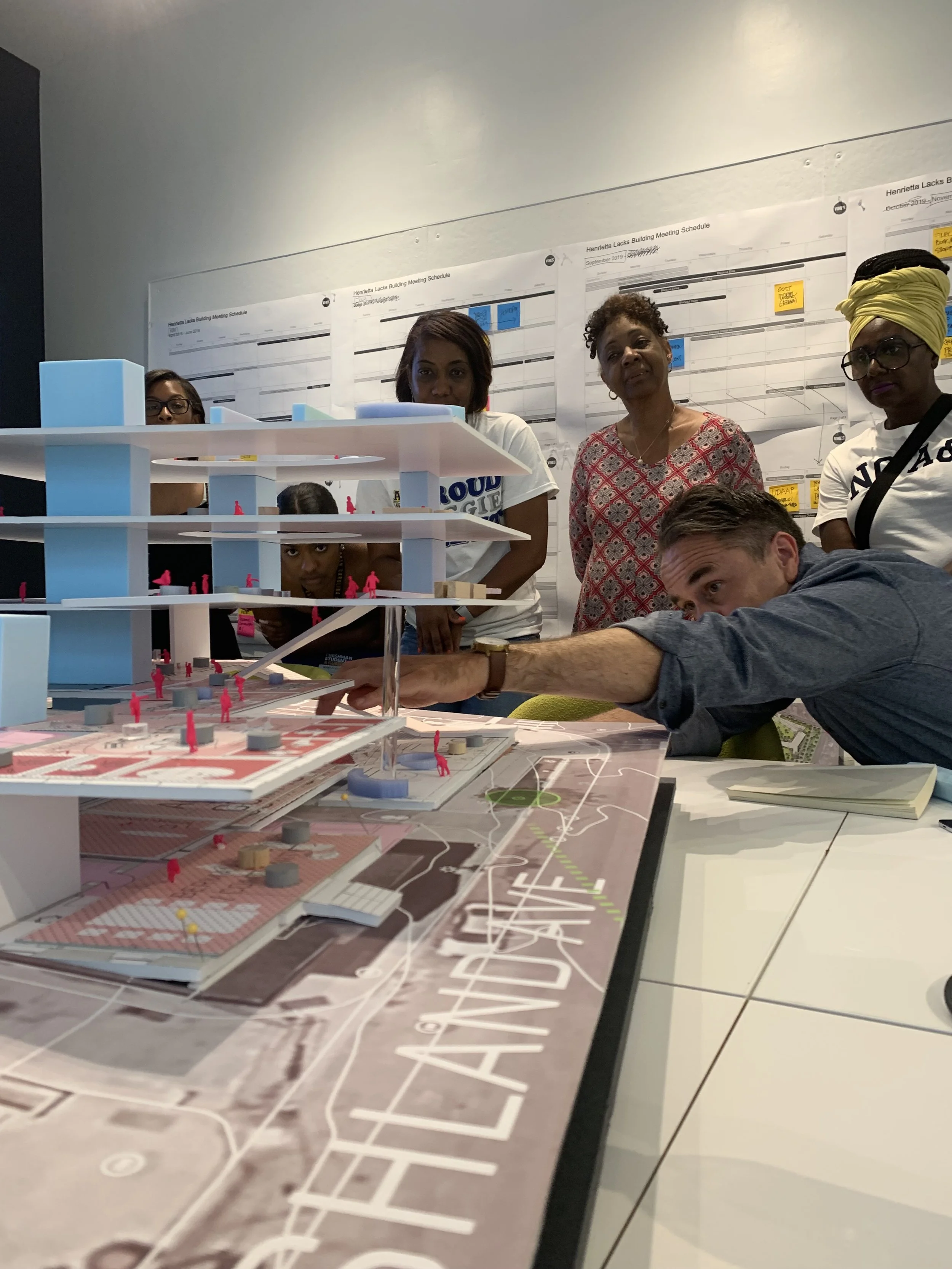 Group of people examining a detailed architectural model on a table in an office or conference room.