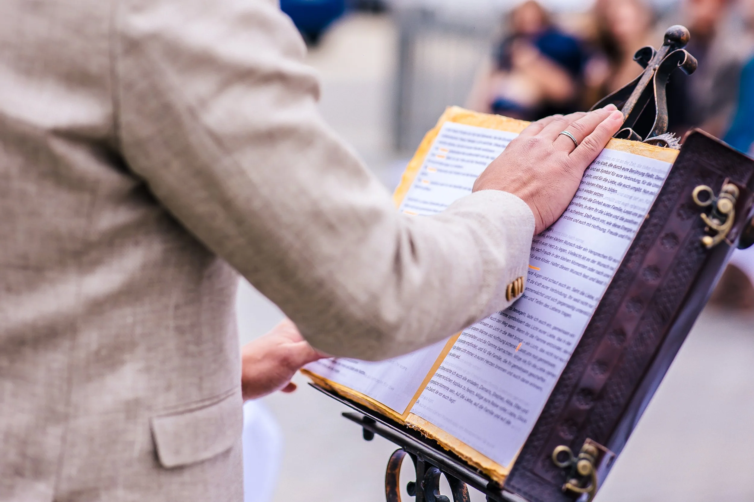 Person liest eine große Papierrolle auf einem Kandelaber, im Hintergrund eine Menschenmenge.