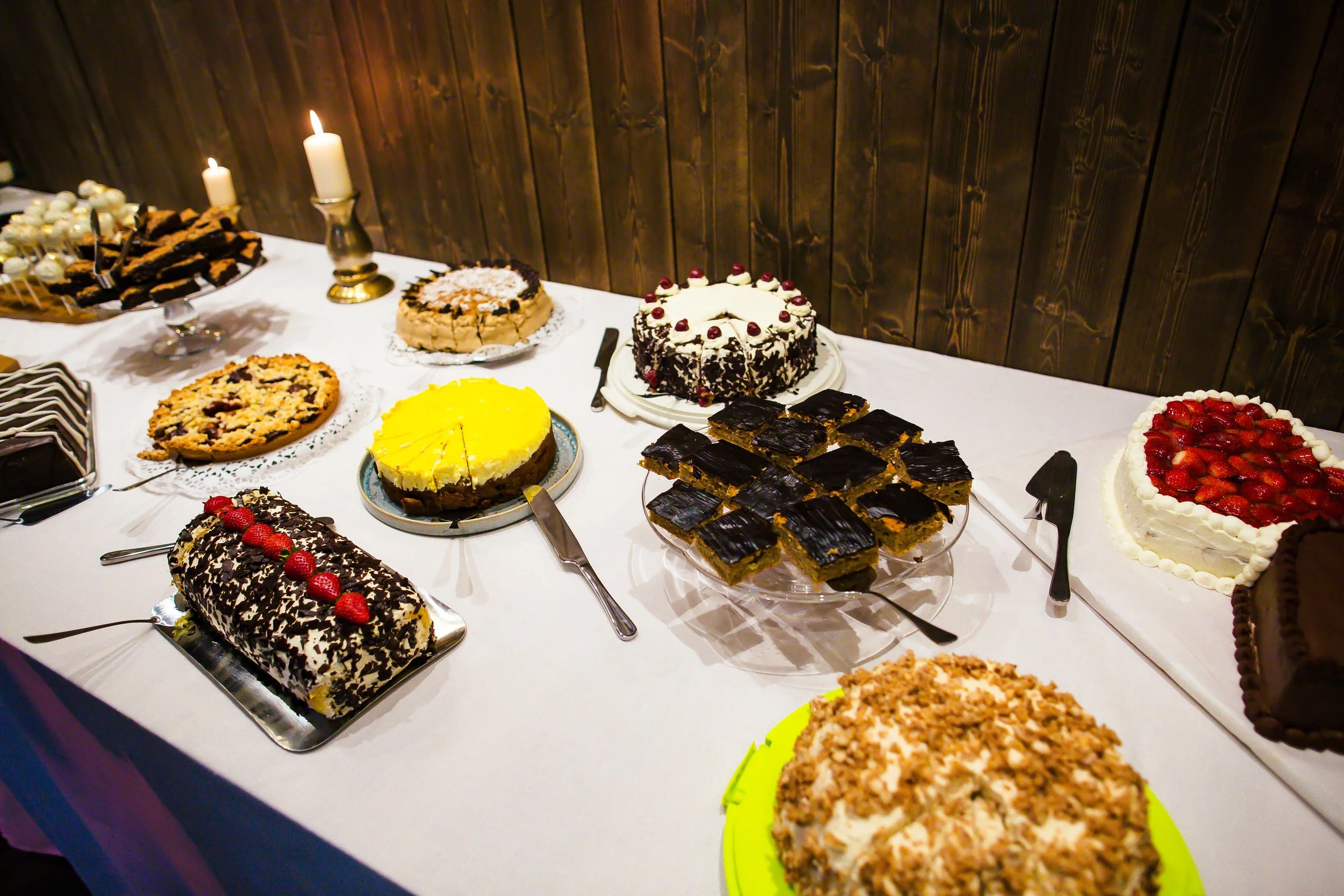 Verschiedene Kuchen und Plätzchen auf einem Festtafel, dekoriert mit Kerzen und serviert auf bunten und silbernen Tellern.