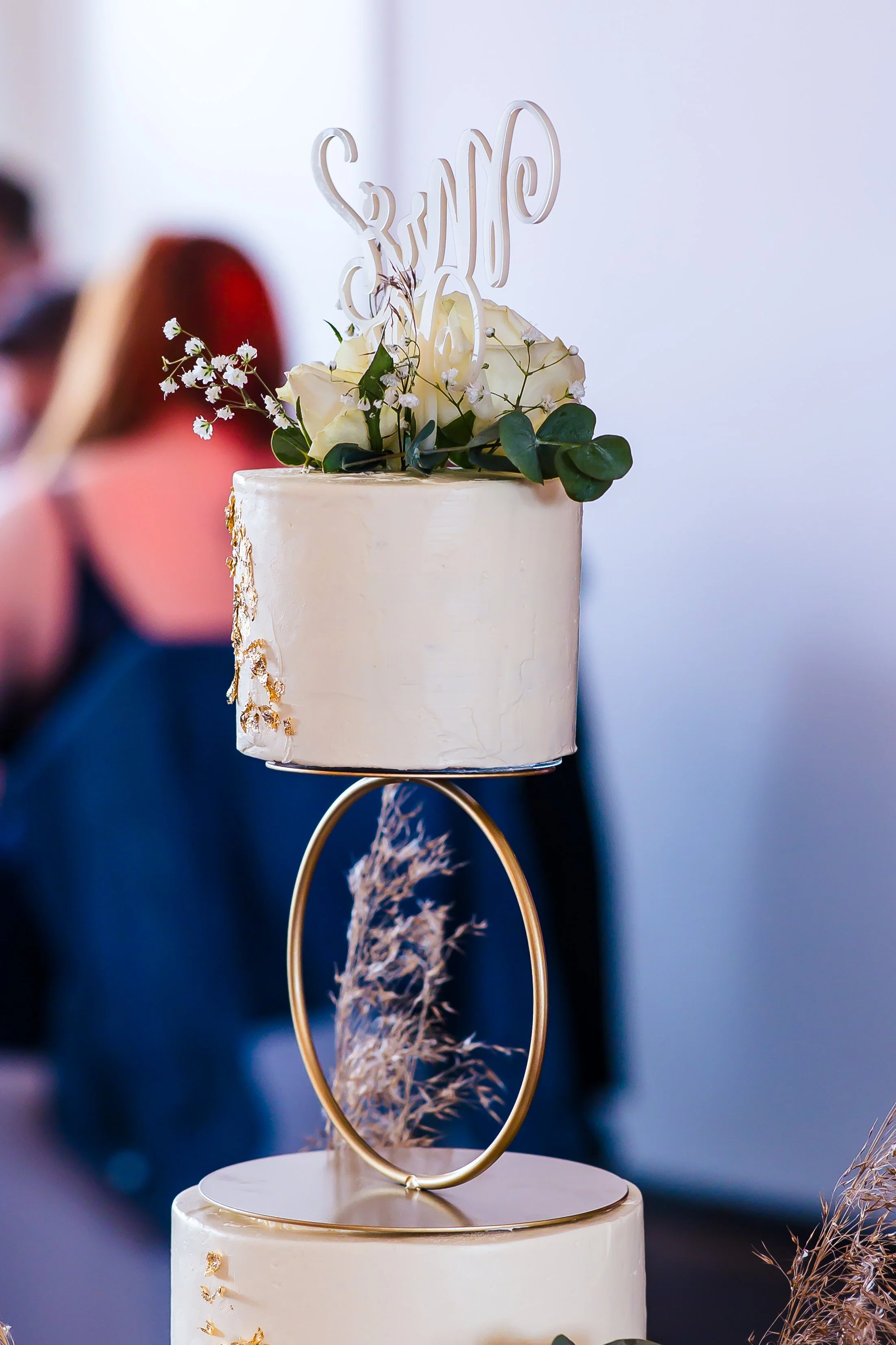 Hochzeitstorte mit weißen Blumen und Goldakzenten, auf einem goldenen Rahmen präsentiert.