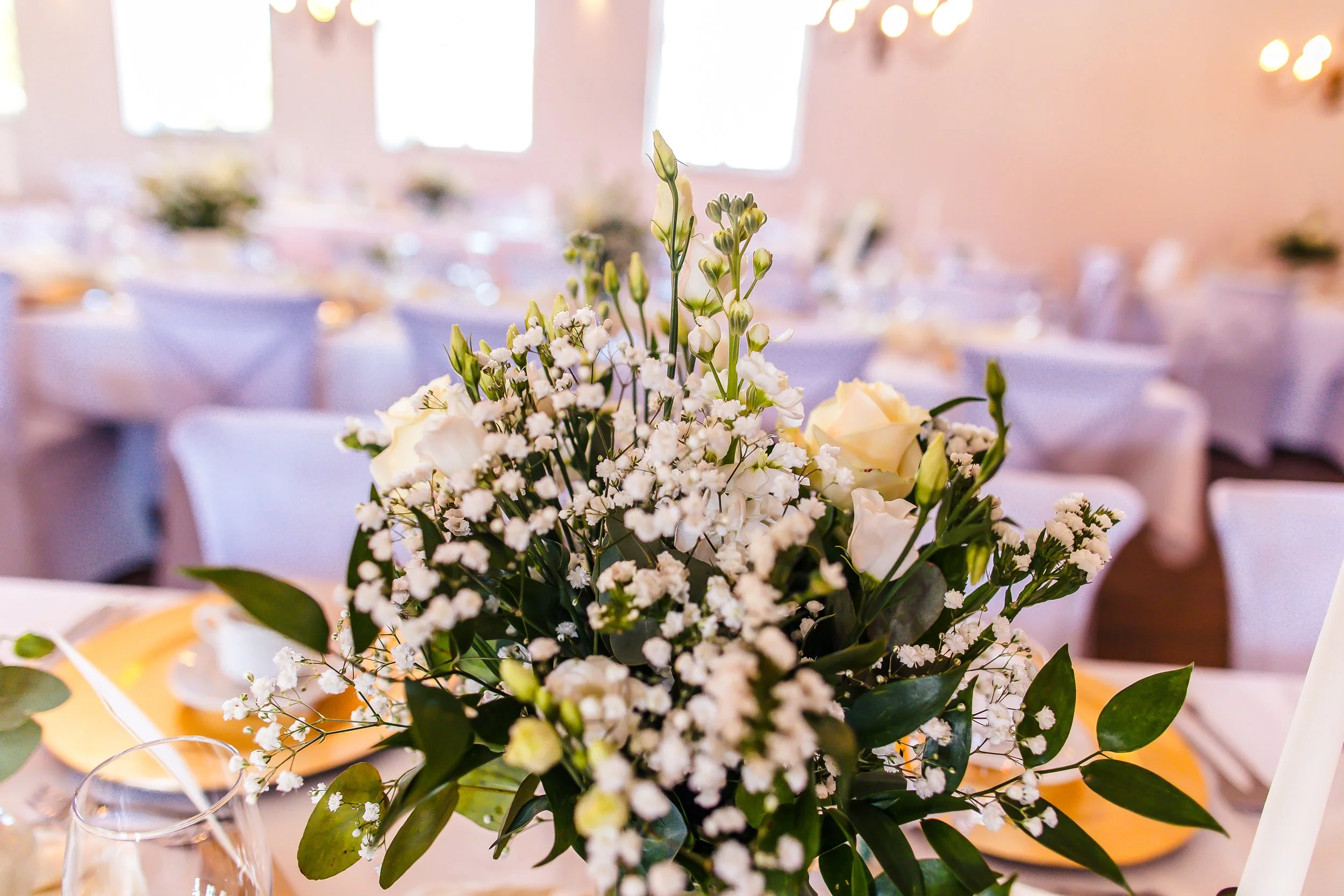 Blumenstrauß aus weißen Rosen, Flieder und Eukalyptus auf festlich gedecktem Tisch bei einer Veranstaltung.