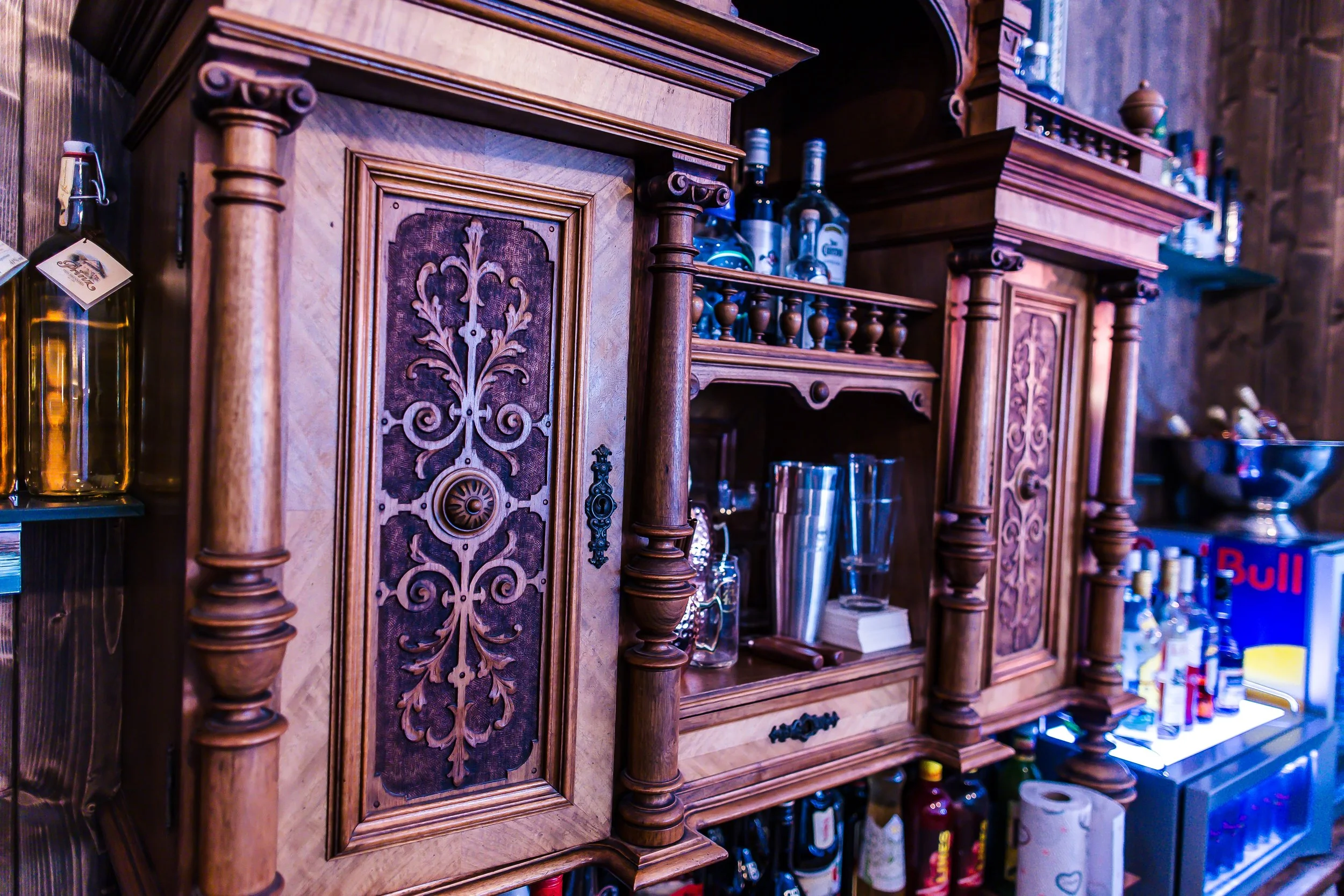 Ein barockes Holzregal mit geschnitzten Verzierungen und Gläsern, Flaschen und Barzubehör darauf, in einer Bar oder Küche.