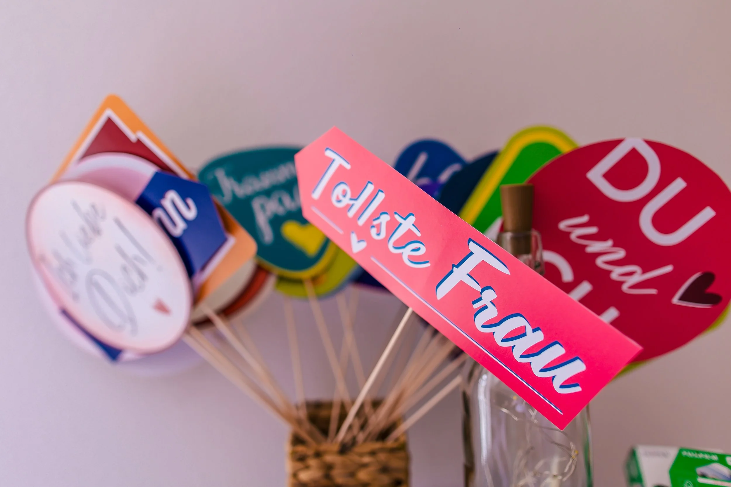 Bunte Wort- und Slogan-Displays auf Schaschlikspießen, die in einem Glas stehen, darunter sind große, bunte Herzausleger mit Sprüchen, die sich auf Liebe und Hochzeit beziehen.