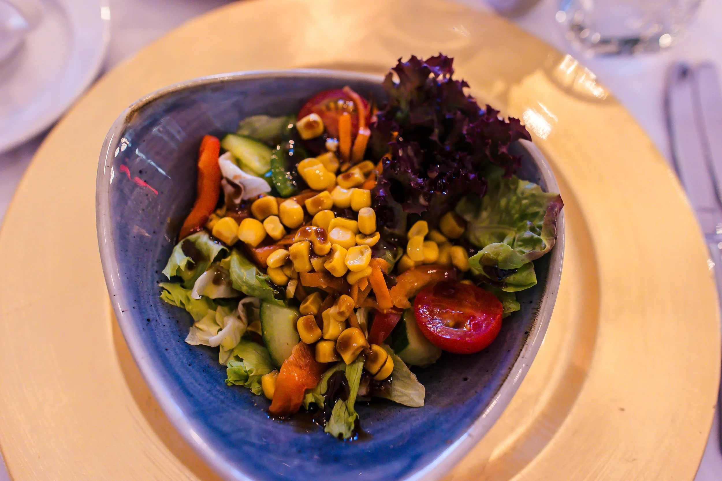 Schüssel mit gemischtem Salat aus Tomaten, Mais, Gurken, Karotten und Blattsalat, serviert auf einem goldenen Teller.