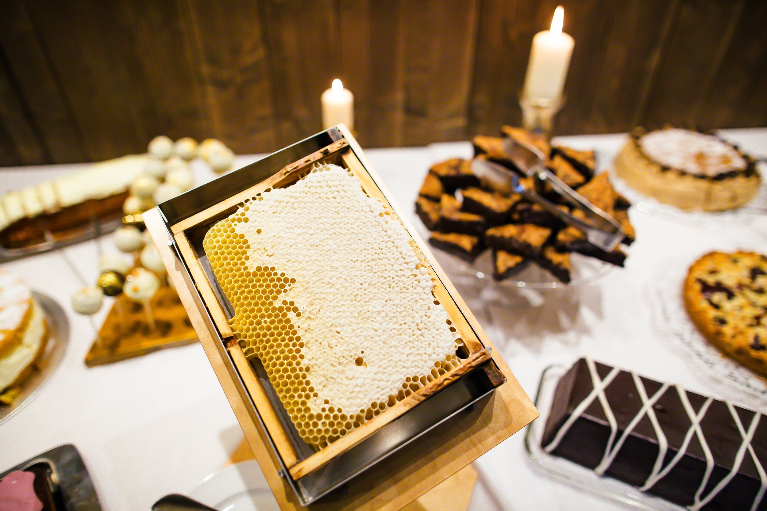 Honigwabe auf einer Schaustation, umgeben von verschiedenen Kuchen und Torten auf einem Tisch bei einer Feier.