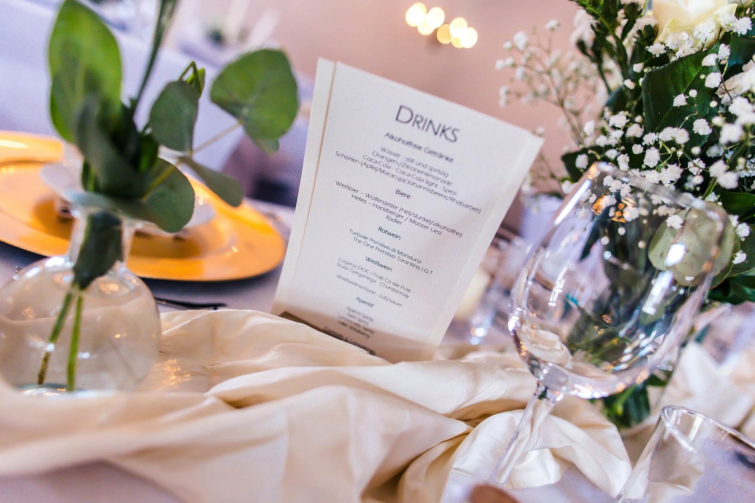 Tischdekoration mit Weingläsern, Blumen und einer Speisekarte auf einem festlich gedeckten Tisch bei einer Feier.