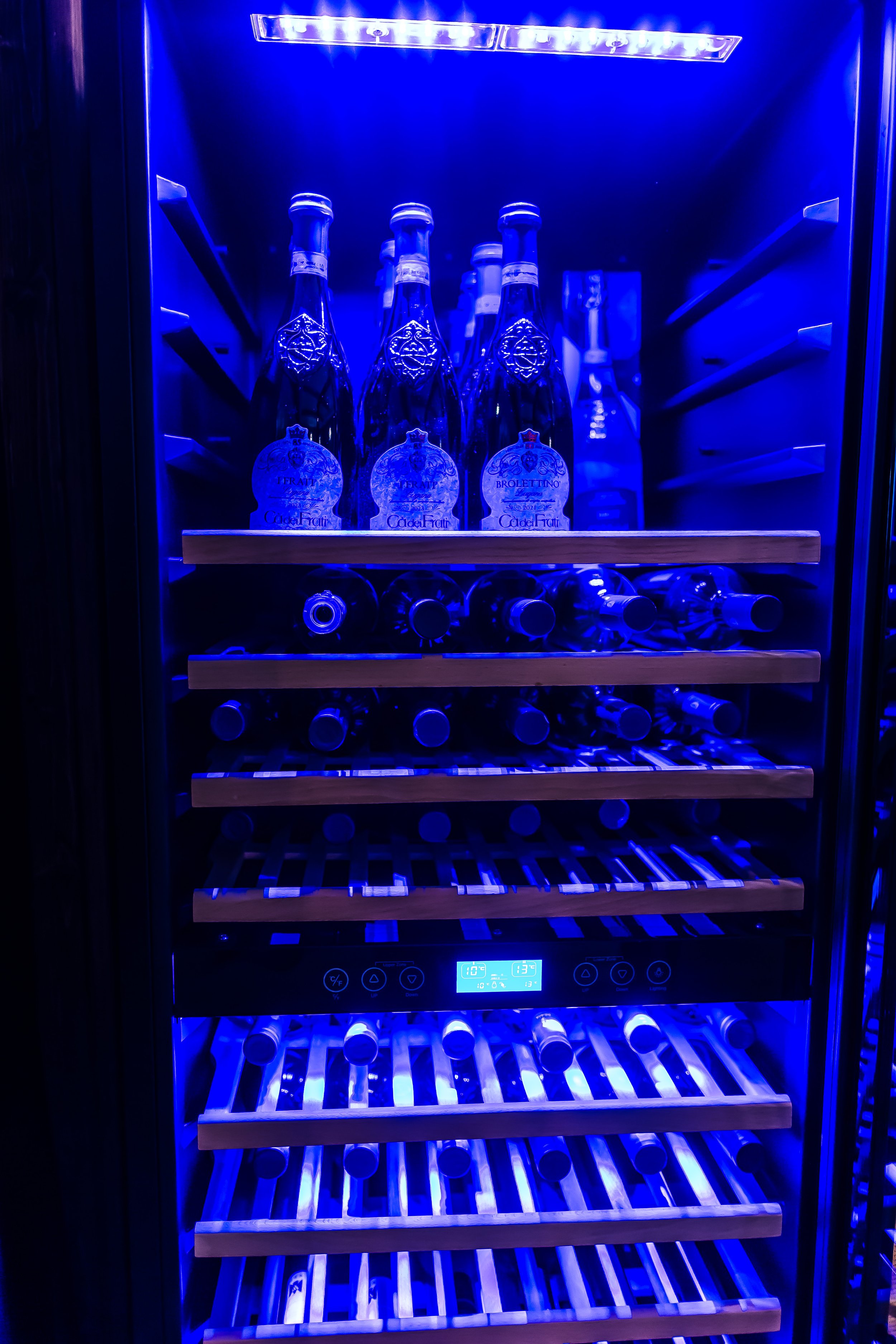 Kühlschrank mit blauer Innenbeleuchtung, voll mit Flaschen und Wasserflaschen, einige auf Holzregalen.