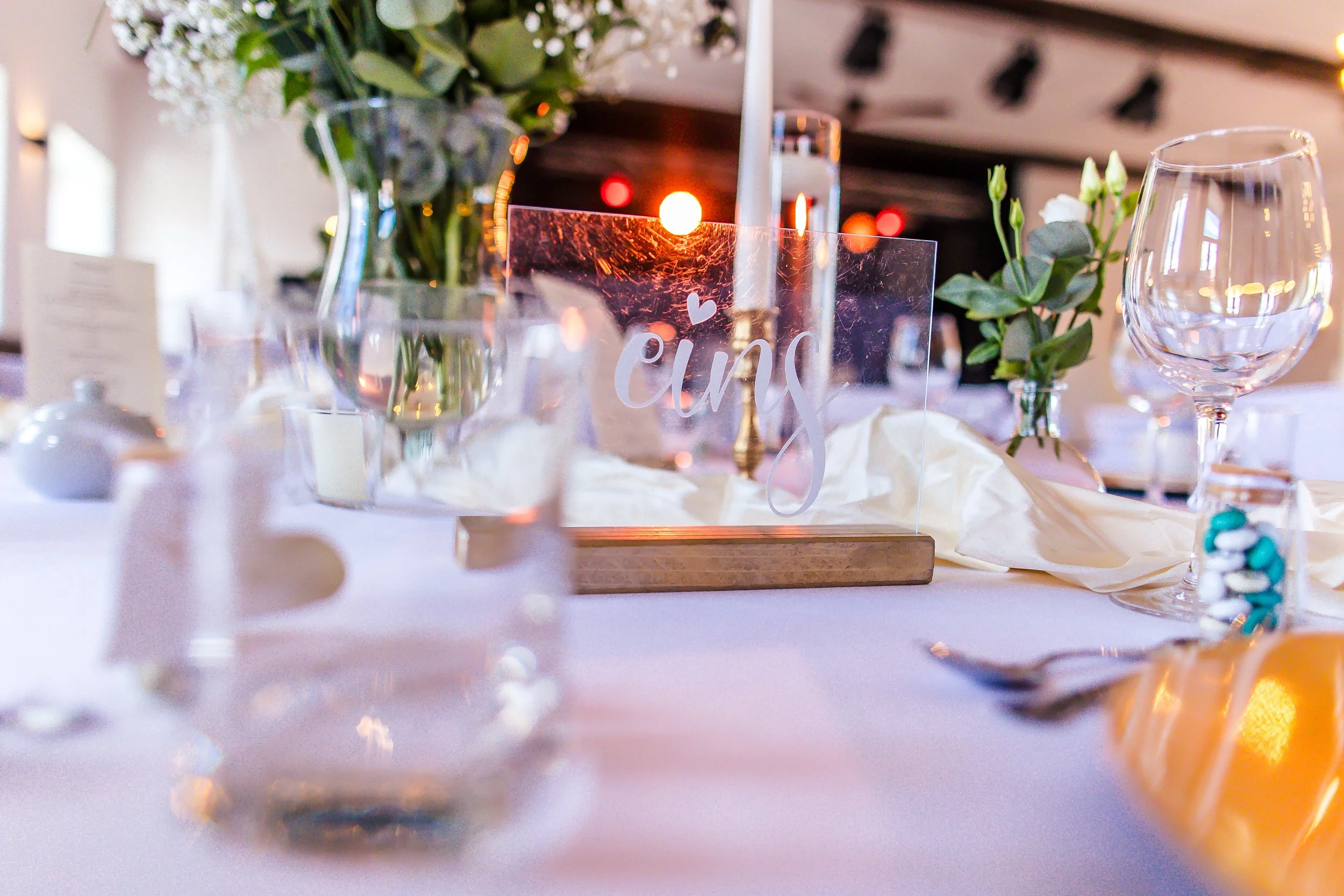 Eleganter festlicher Tisch mit Blumen, Gläsern und einem Tischschild mit der Aufschrift »eins« bei einer Feier.