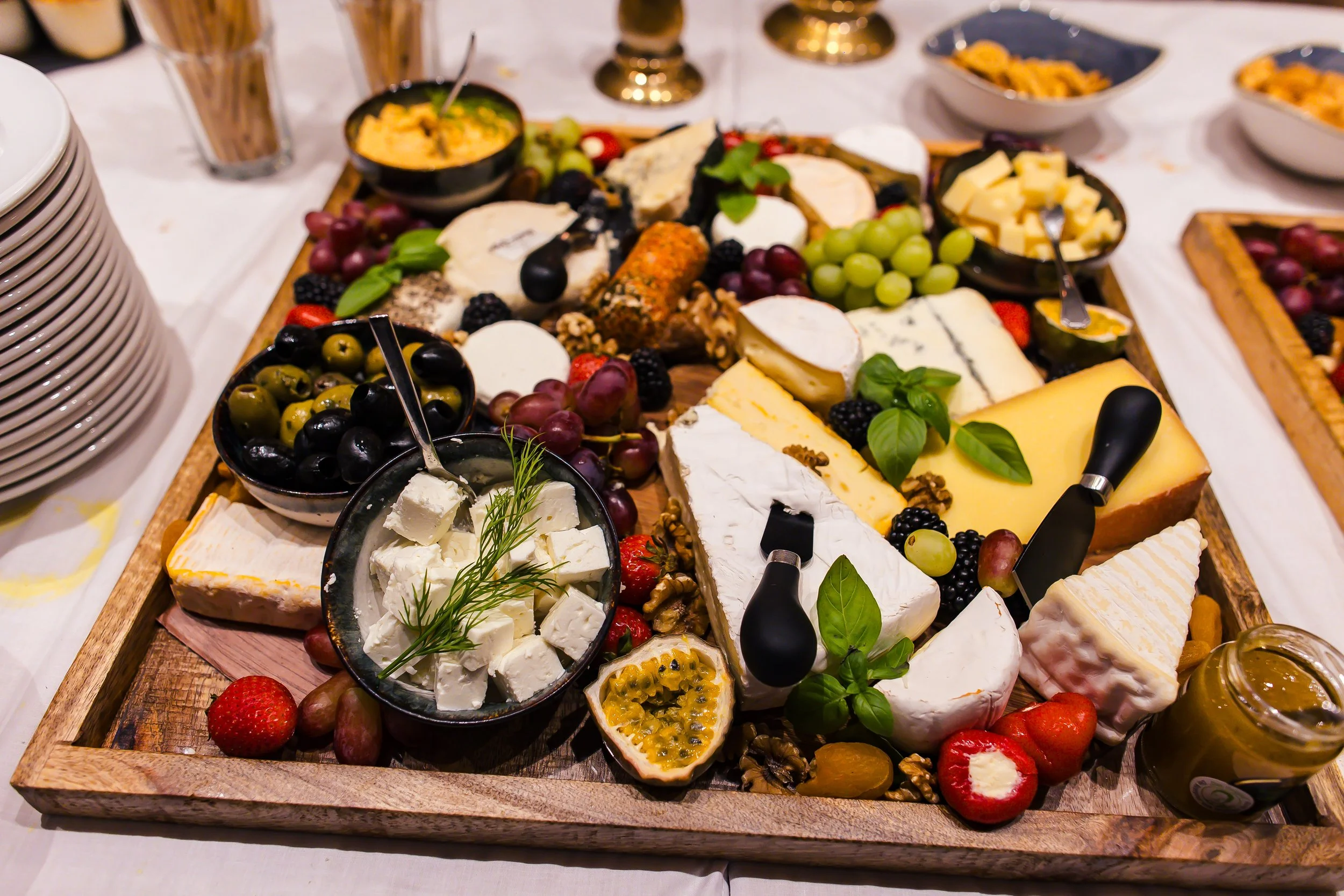 Käseplatte mit verschiedenen Käsesorten, Früchten wie Trauben, Erdbeeren und Passionsfrucht, Oliven, Erdbeeren, Nüssen und Honig, serviert auf einem Holztablett.