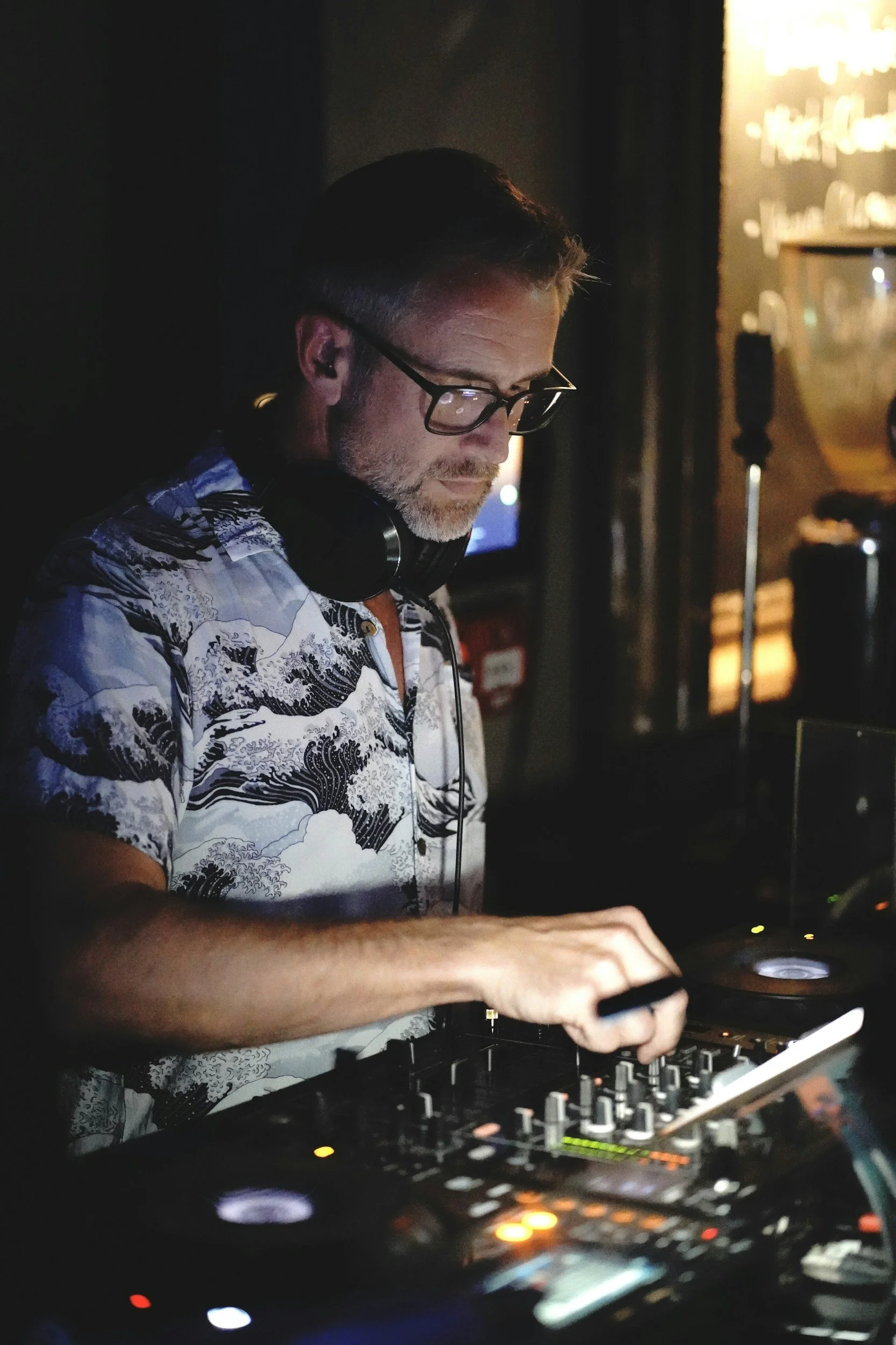 Ein Mann mit Brille und Kopfhörer in einem dunklen Raum, der an einem DJ-Controller arbeitet.