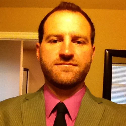 Man in a green suit with pink shirt and black tie taking a selfie indoors.