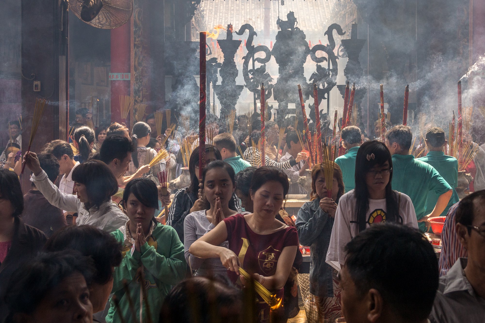 Menschen in einem Tempel bei einer traditionellen Zeremonie, viele halten Räucherstäbchen, Rauch und zeremonielle Gegenstände sichtbar.